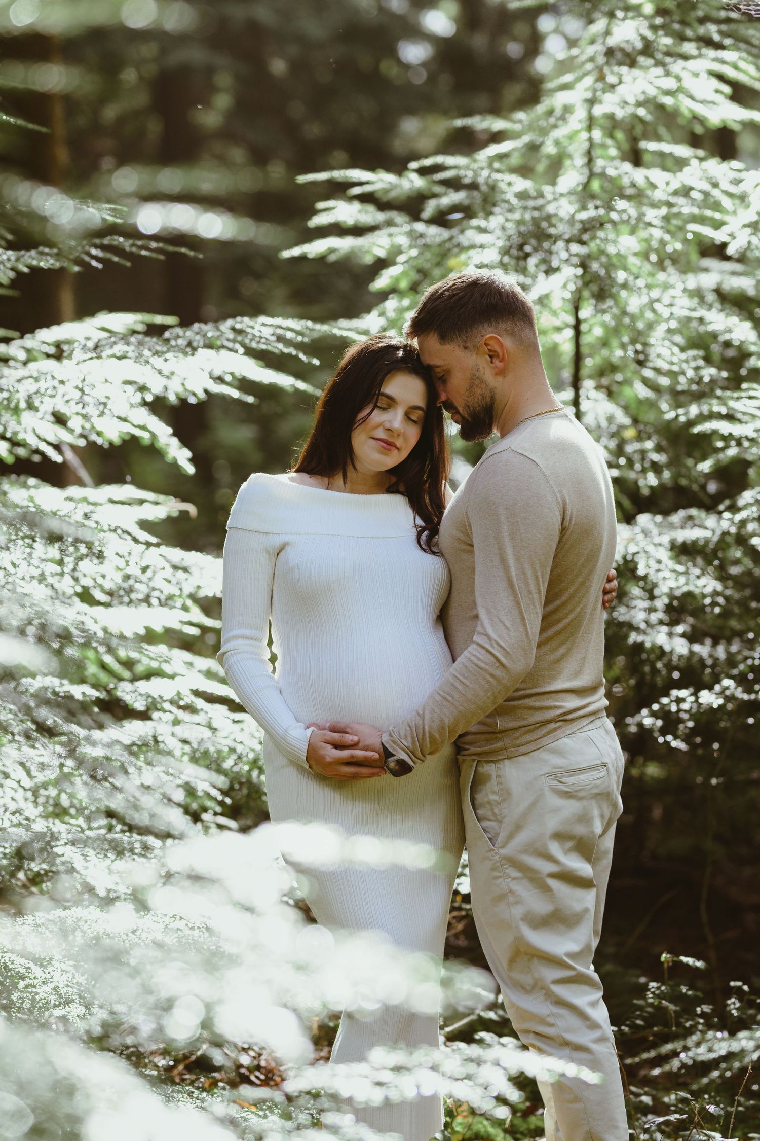 A winter maternity session featuring a couple in coordinating neutral outfits among snow-dusted trees.