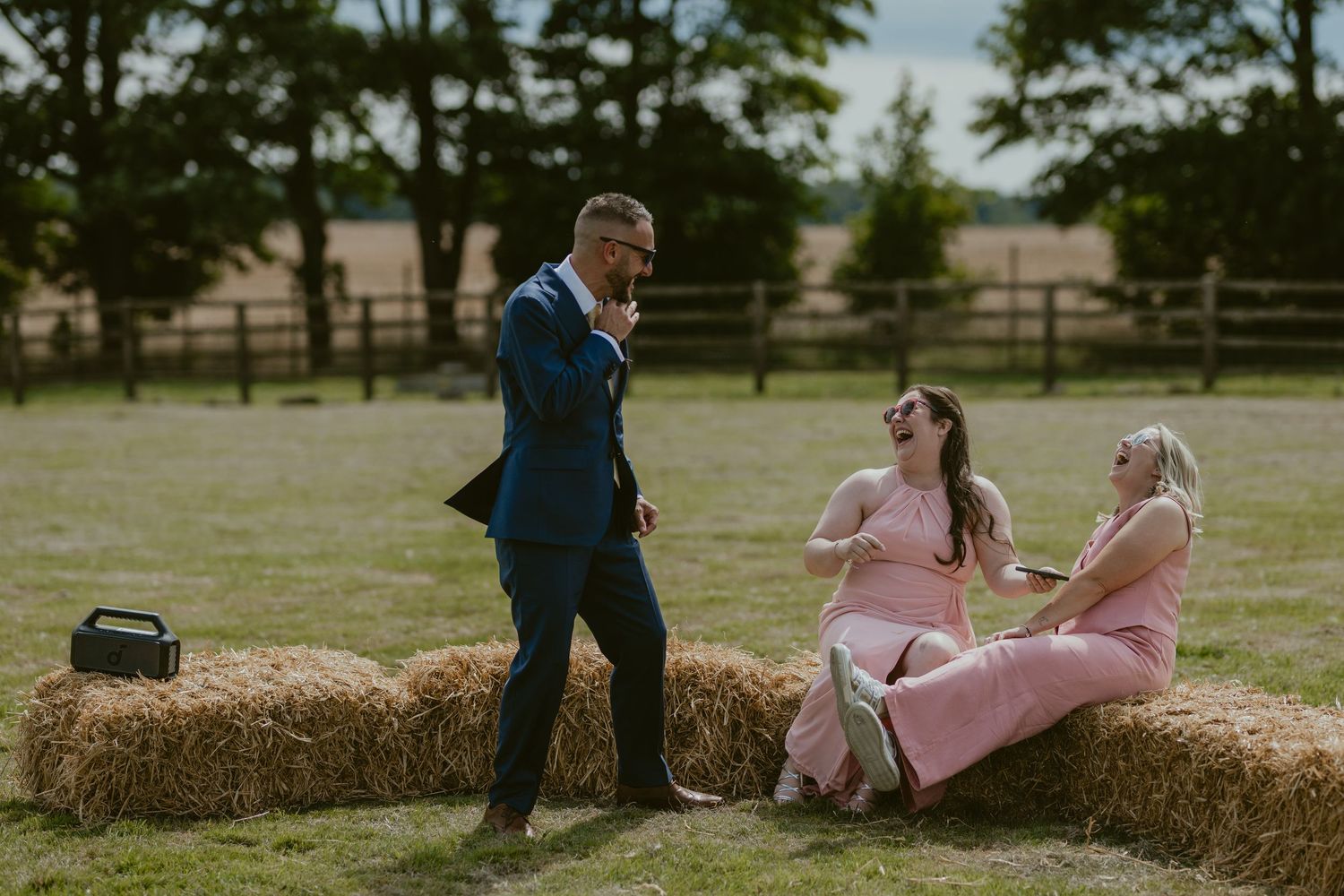 Wedding guests in pink and blue attire chatting on hay bales.