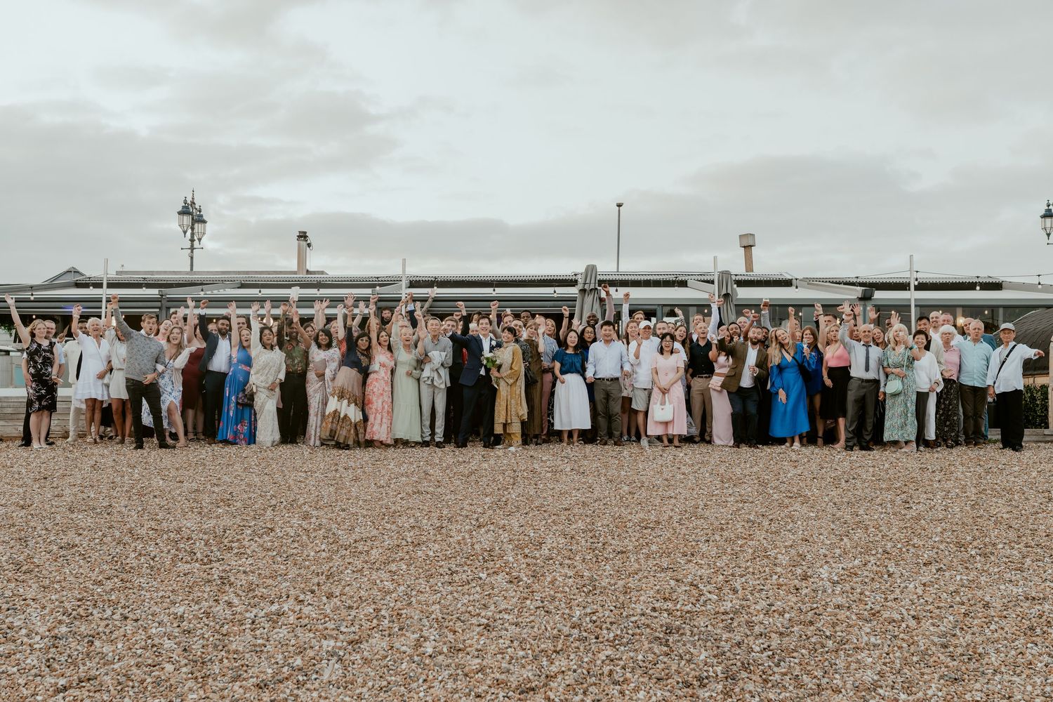 Panoramic view of wedding guests gathered on a beach with mountains in the background.