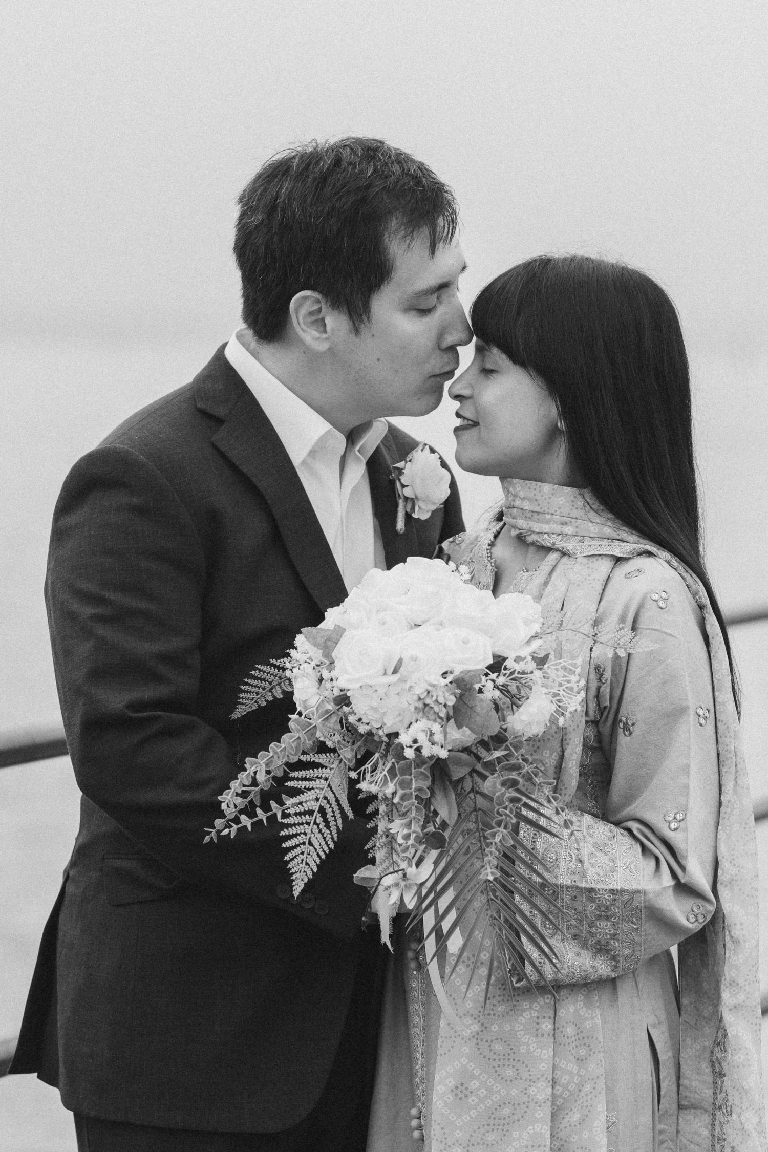 Romantic couple sharing tender moments with white floral bouquet against neutral background.