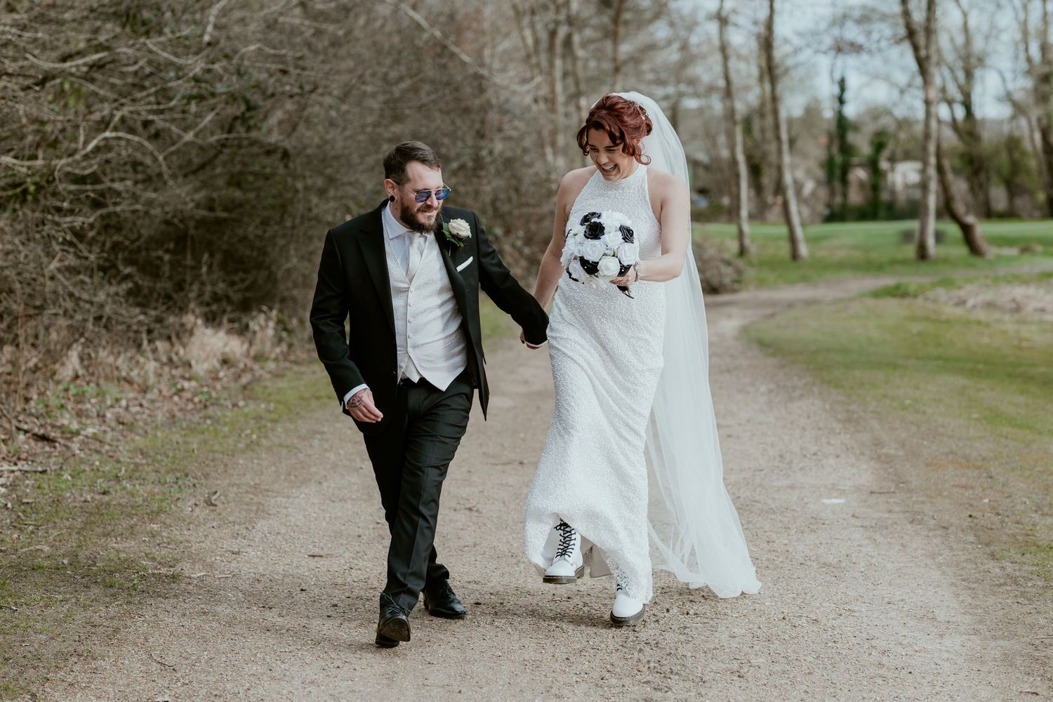 Couple walking together on a tree-lined dirt path in formal attire.