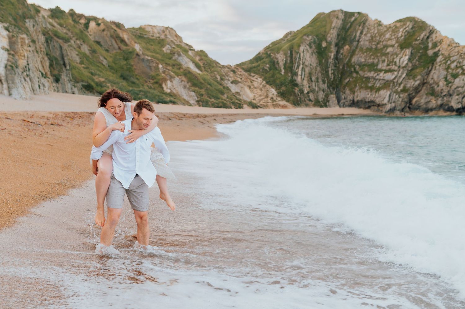 A couple walks along a scenic beach surrounded by dramatic coastal cliffs.