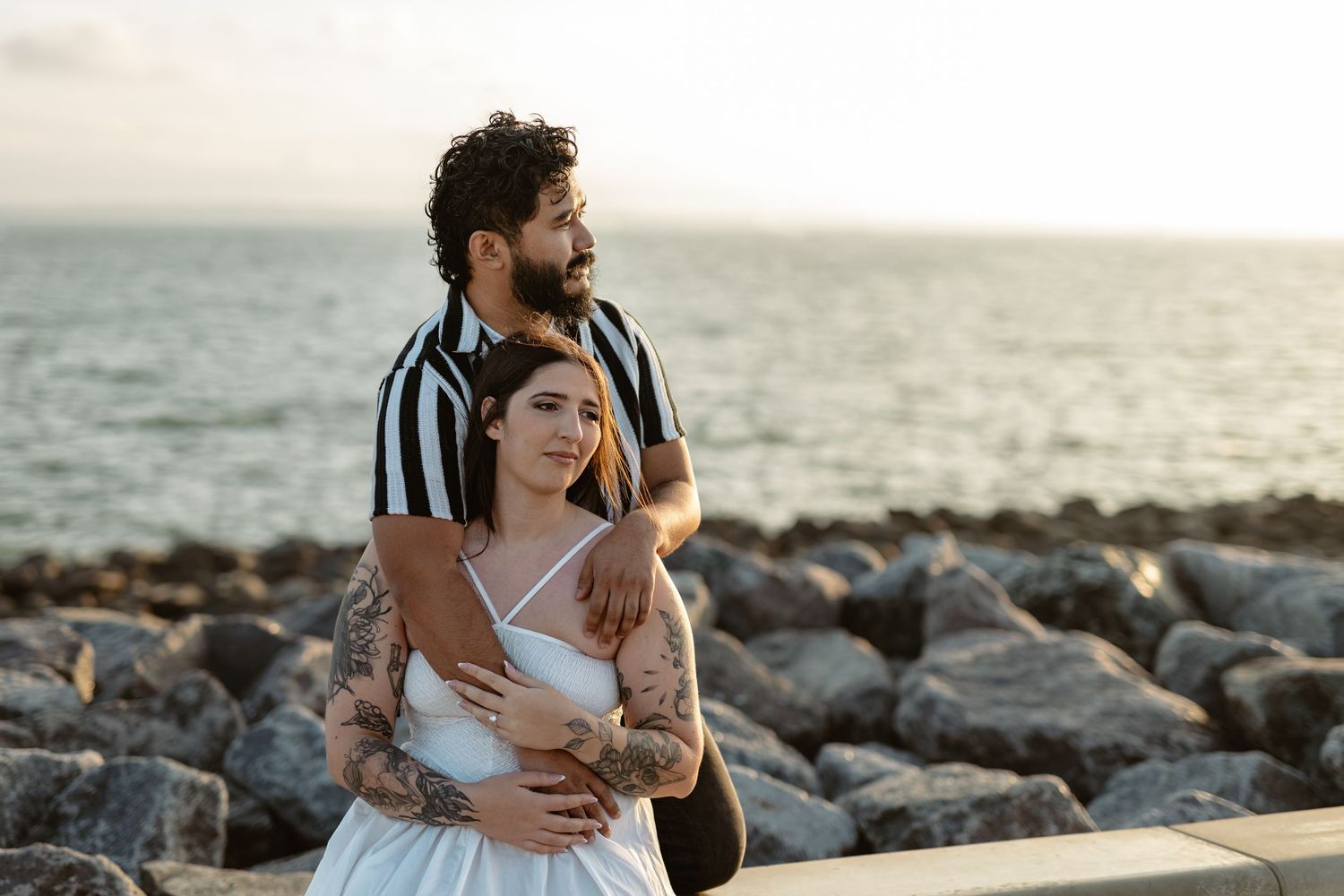 A couple embraces on rocky coastal shore during golden hour.