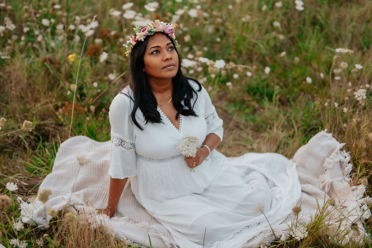 Woman in white dress sitting gracefully in a wildflower field during golden hour.