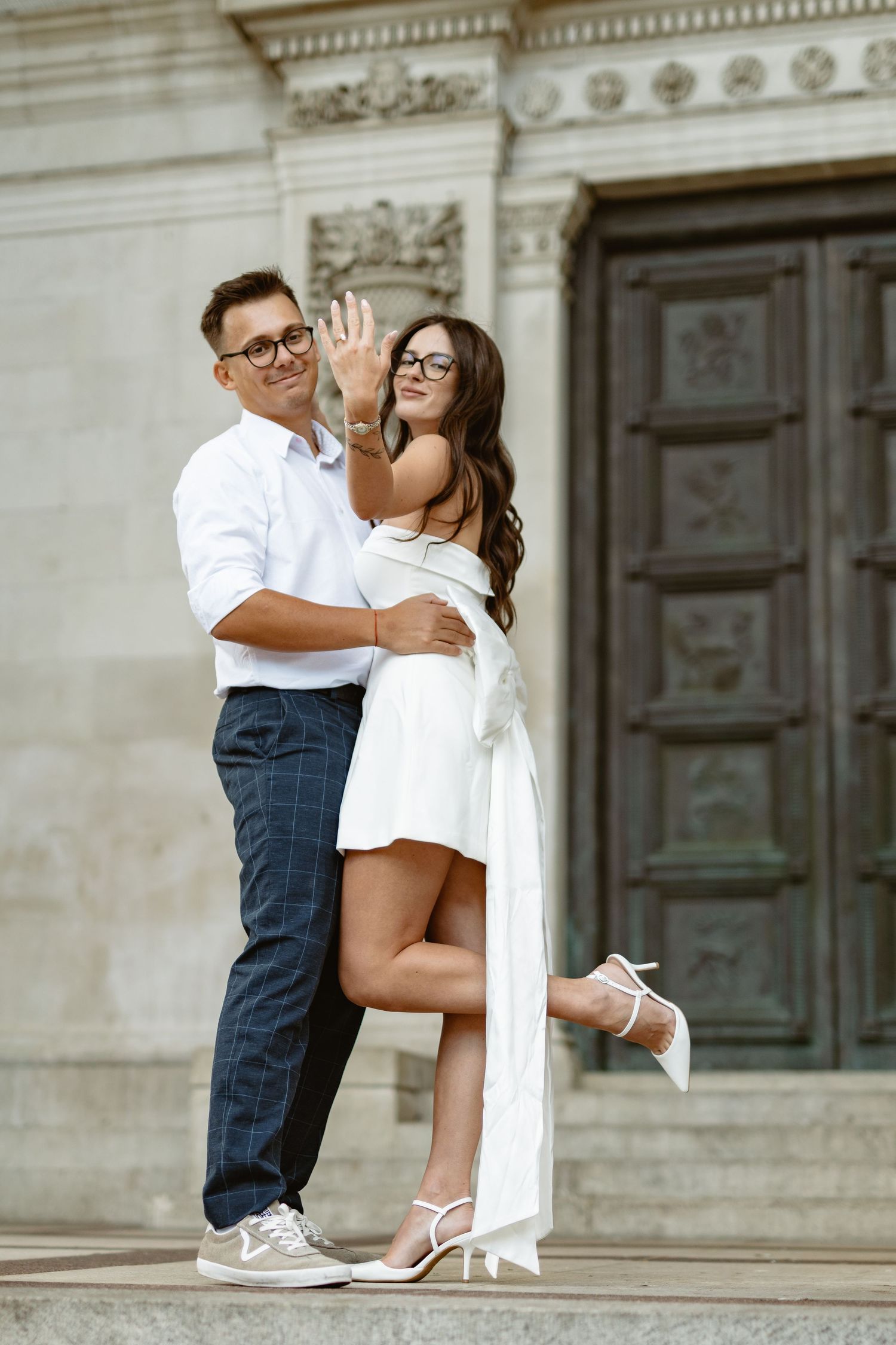 Elegant couple poses together on ornate stone steps near decorative architectural details.