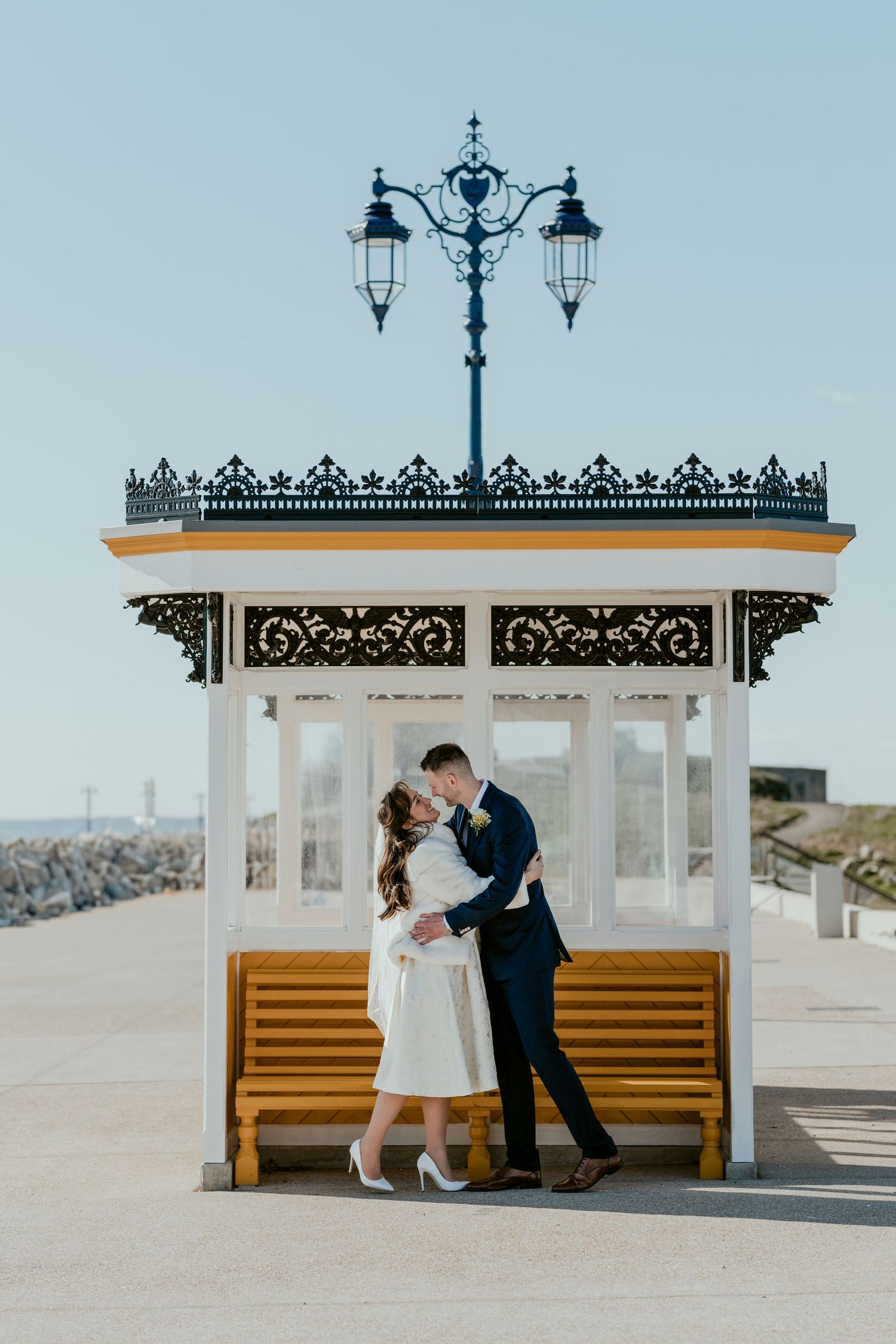 Romantic moment shared at vintage seaside shelter with wooden bench and ornate details.