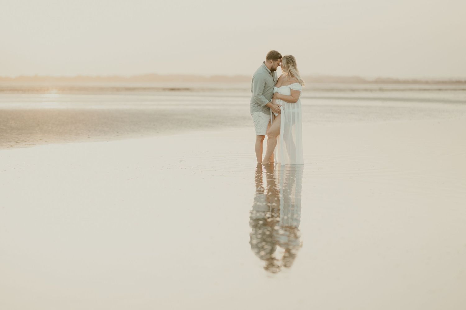 Couple embracing on a misty beach at sunset in soft romantic lighting.
