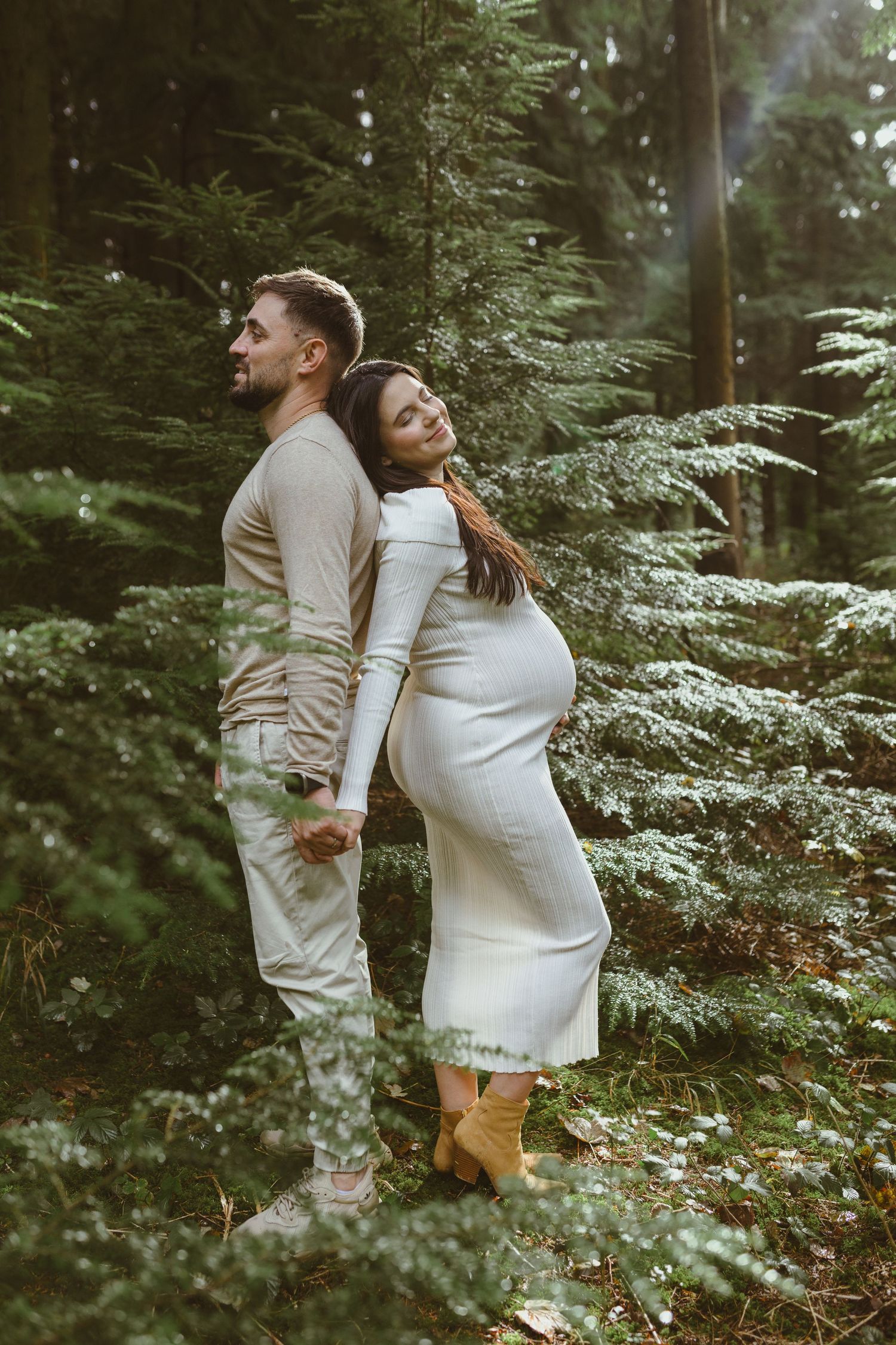 Intimate maternity moment captured in green forest setting.