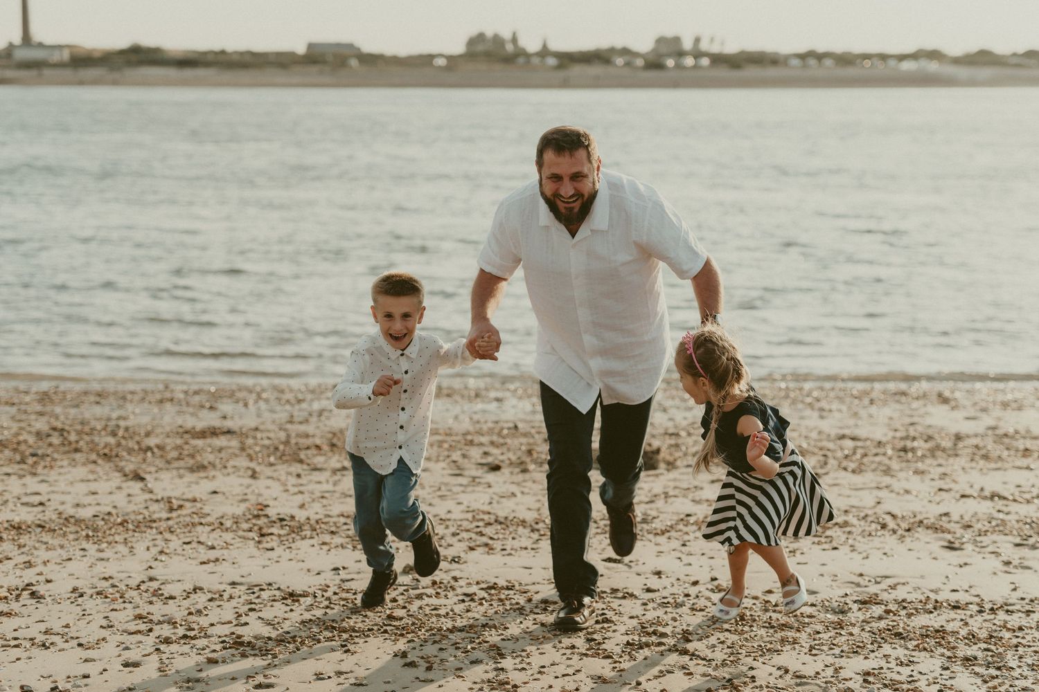 Family walking together on a sandy beach at sunset with waves in the background.