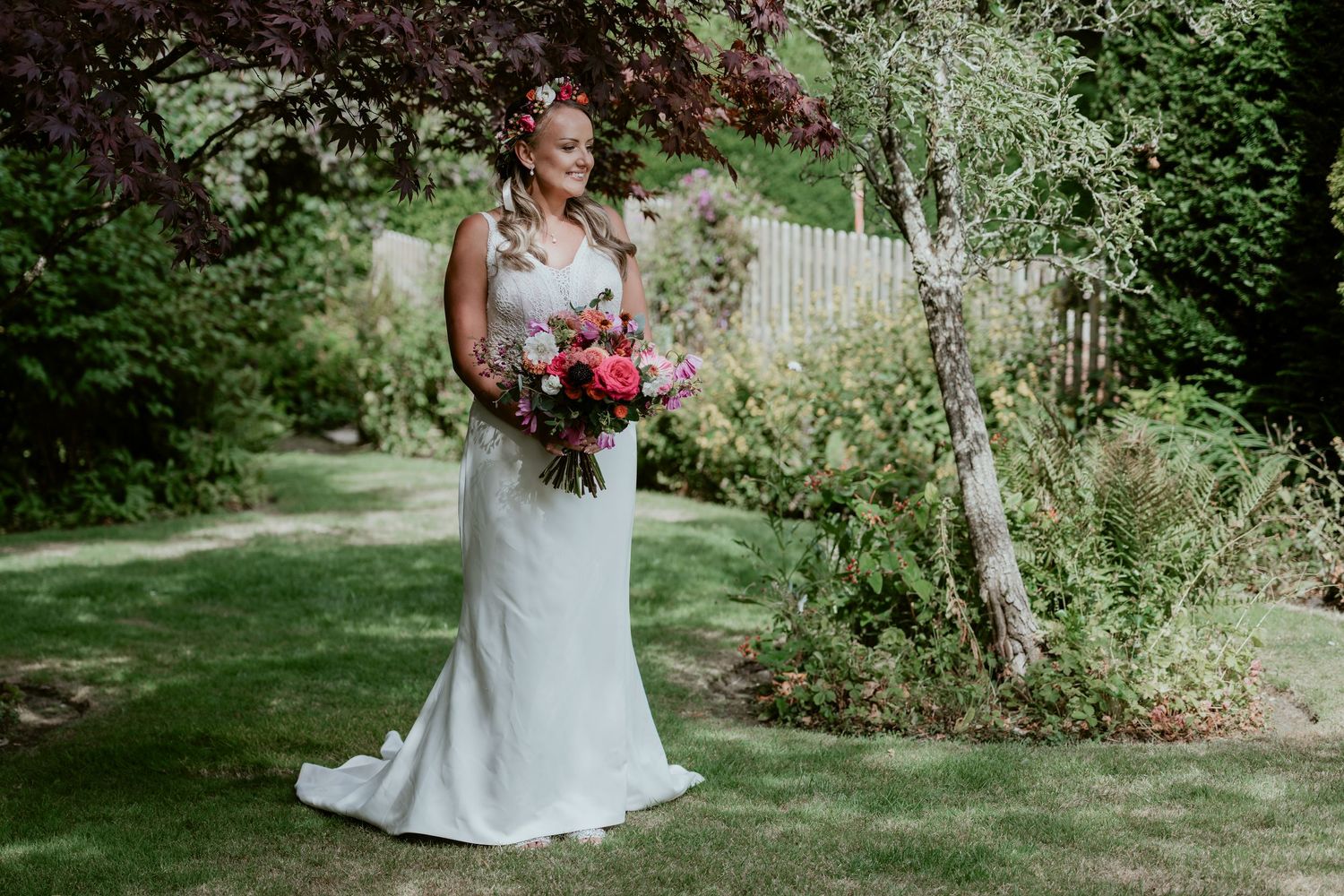 Wedding party poses in front of lush greenery and gardens on a sunny day.