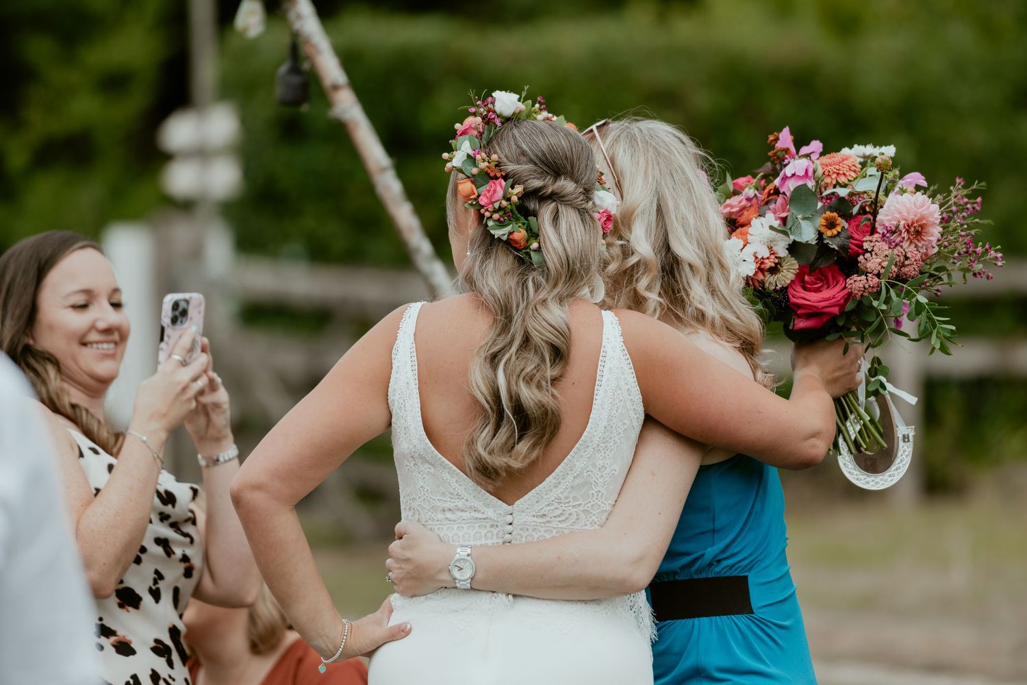 Wedding guests taking photos and embracing during outdoor celebration.