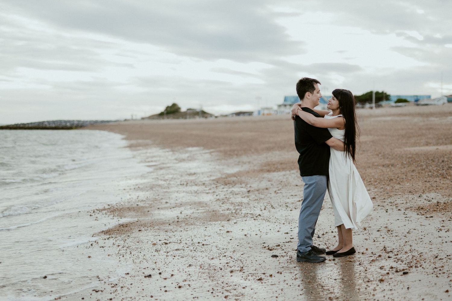 Two people walk together along a serene beach shoreline at dusk.