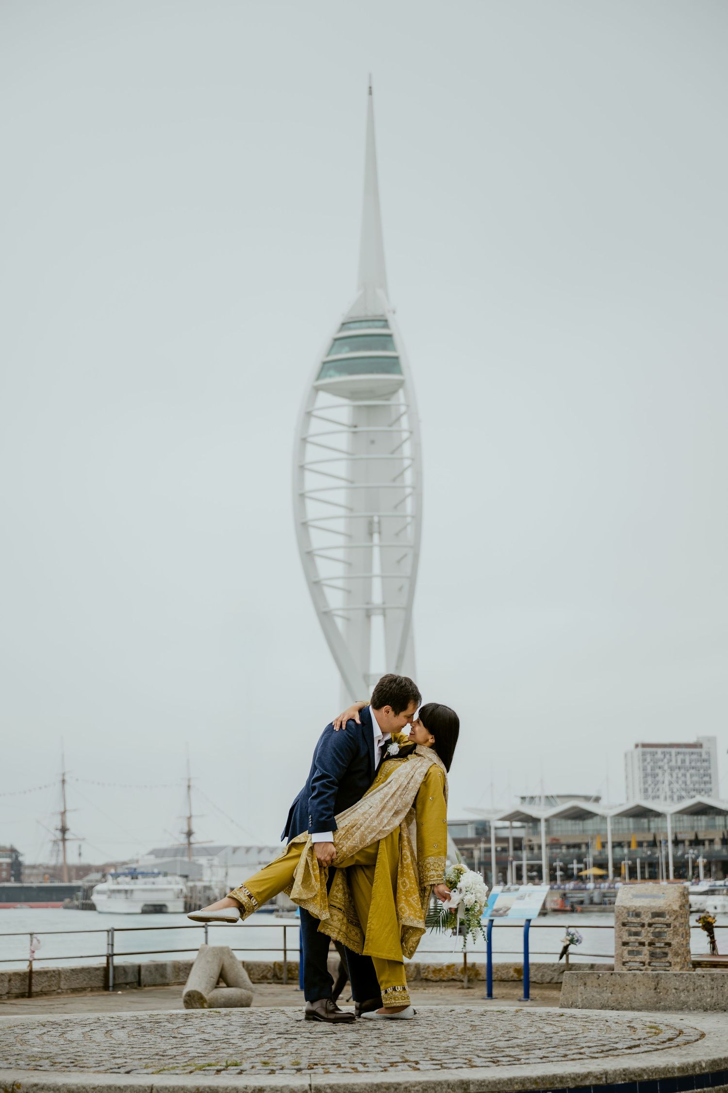 A romantic moment in front of Portsmouth's Spinnaker Tower on a cloudy day.