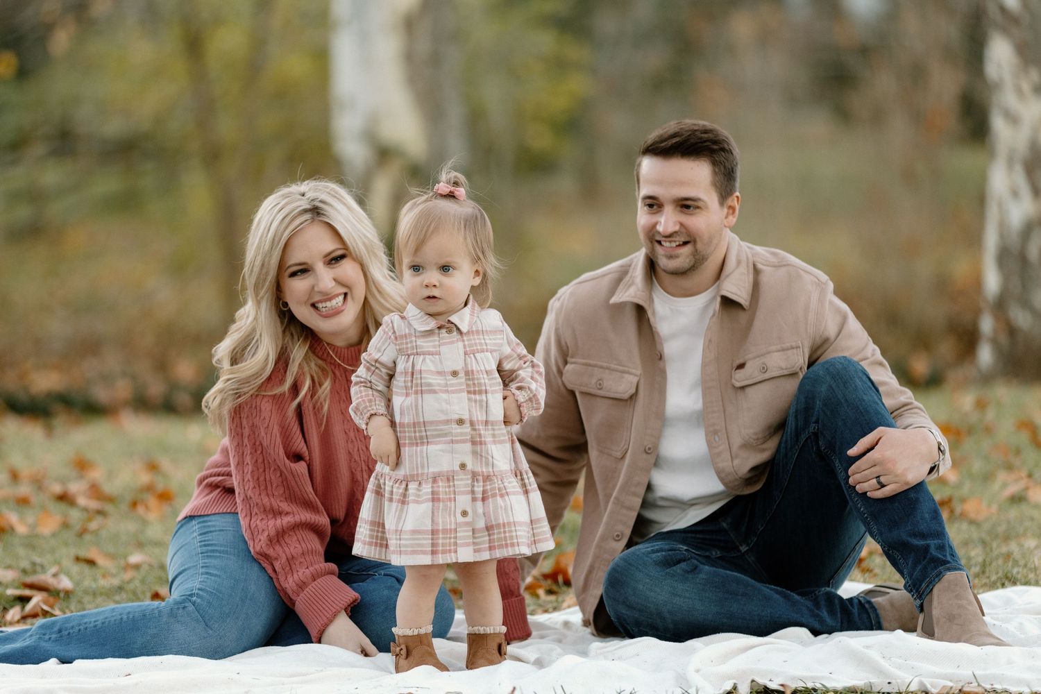 Family sitting together on a blanket outdoors during autumn with fallen leaves around them.