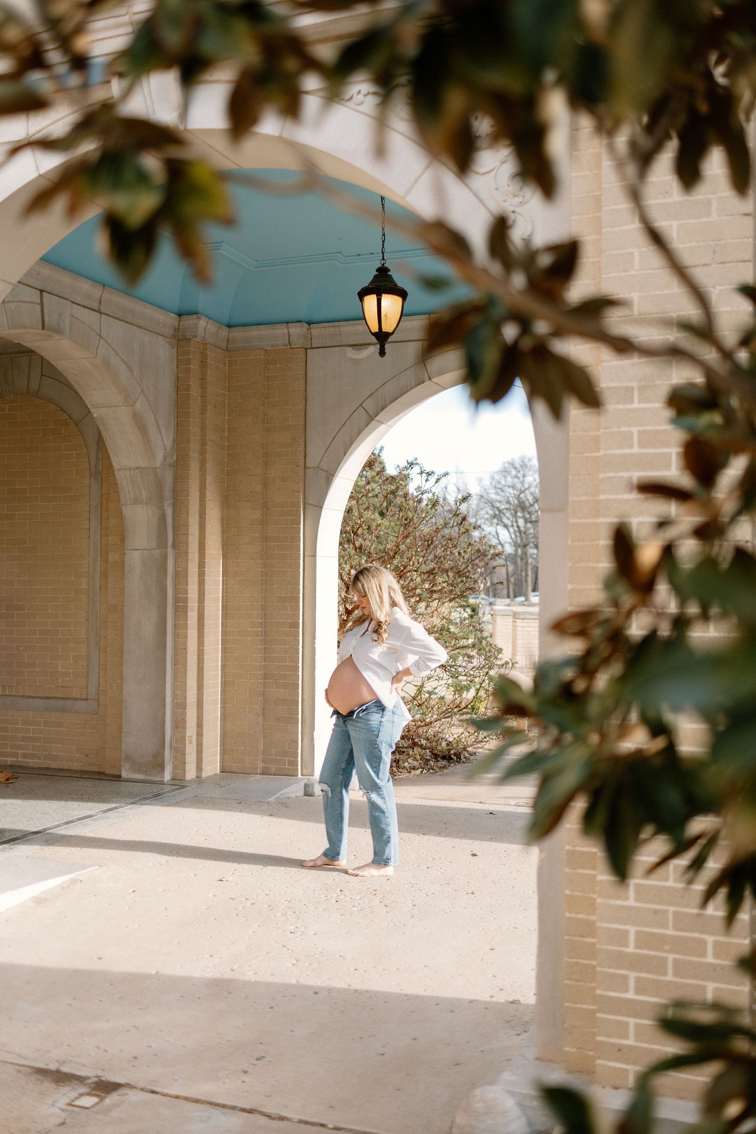 A person stands under stone archways along a covered walkway with sunlight casting dramatic shadows.