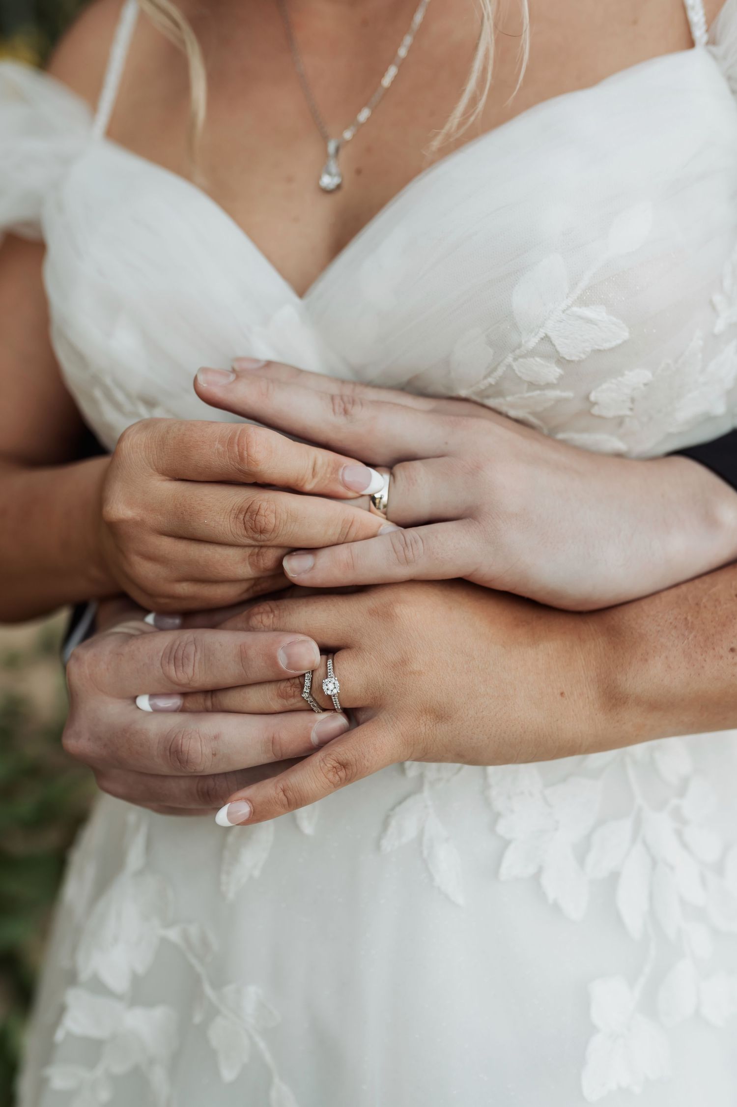 Newlywed couple displaying wedding rings, bride in white lace gown with diamond engagement ring and groom embracing her.