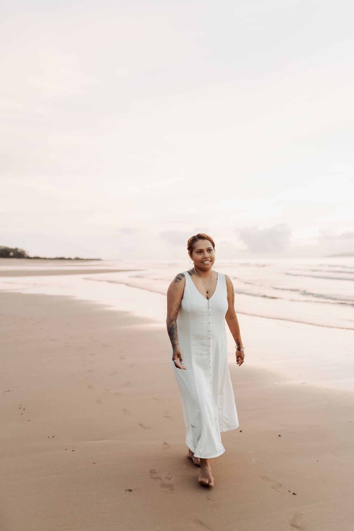 Person wearing a white dress walking along a serene beach at sunset.