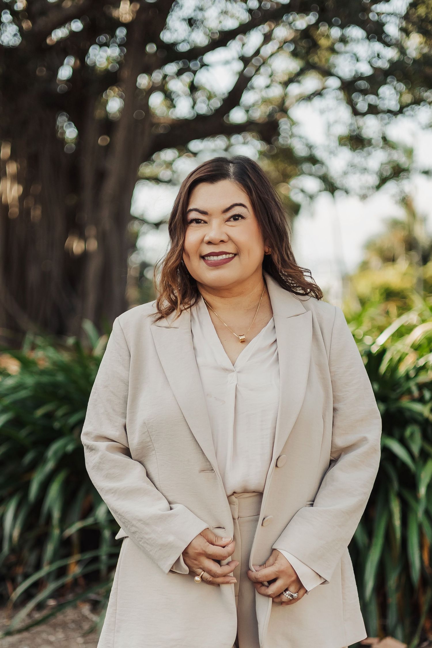 Professional portrait in a cream blazer against a garden background.