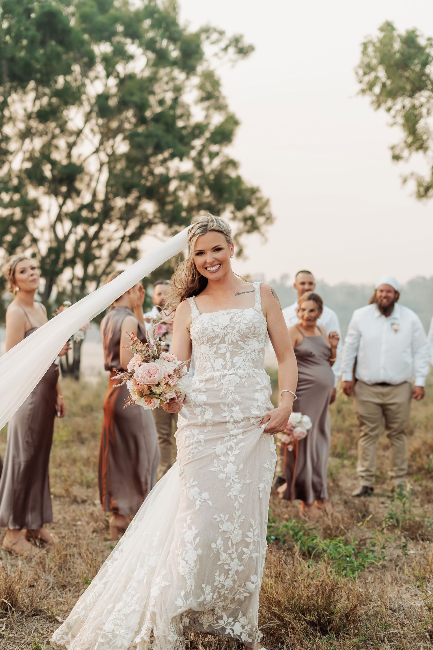 Wedding party celebrating in a rustic outdoor setting with bridesmaids in taupe dresses.
