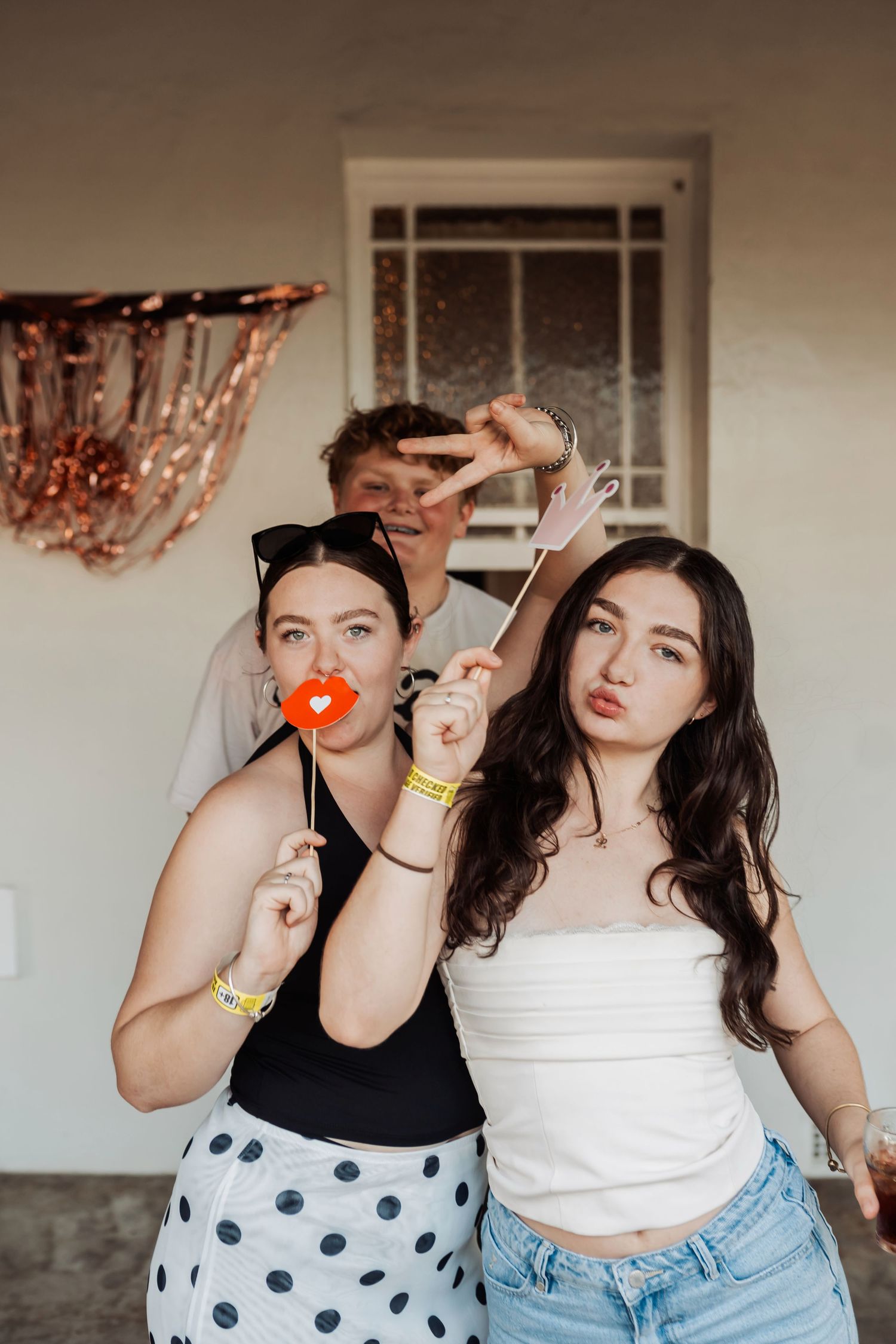Young people posing with party props against a wall with festive copper decorations.
