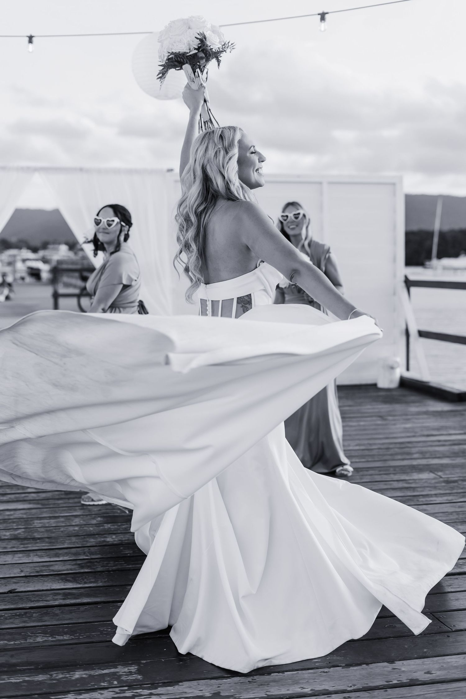 Flowing white wedding dress twirls on wooden deck in black and white photography.