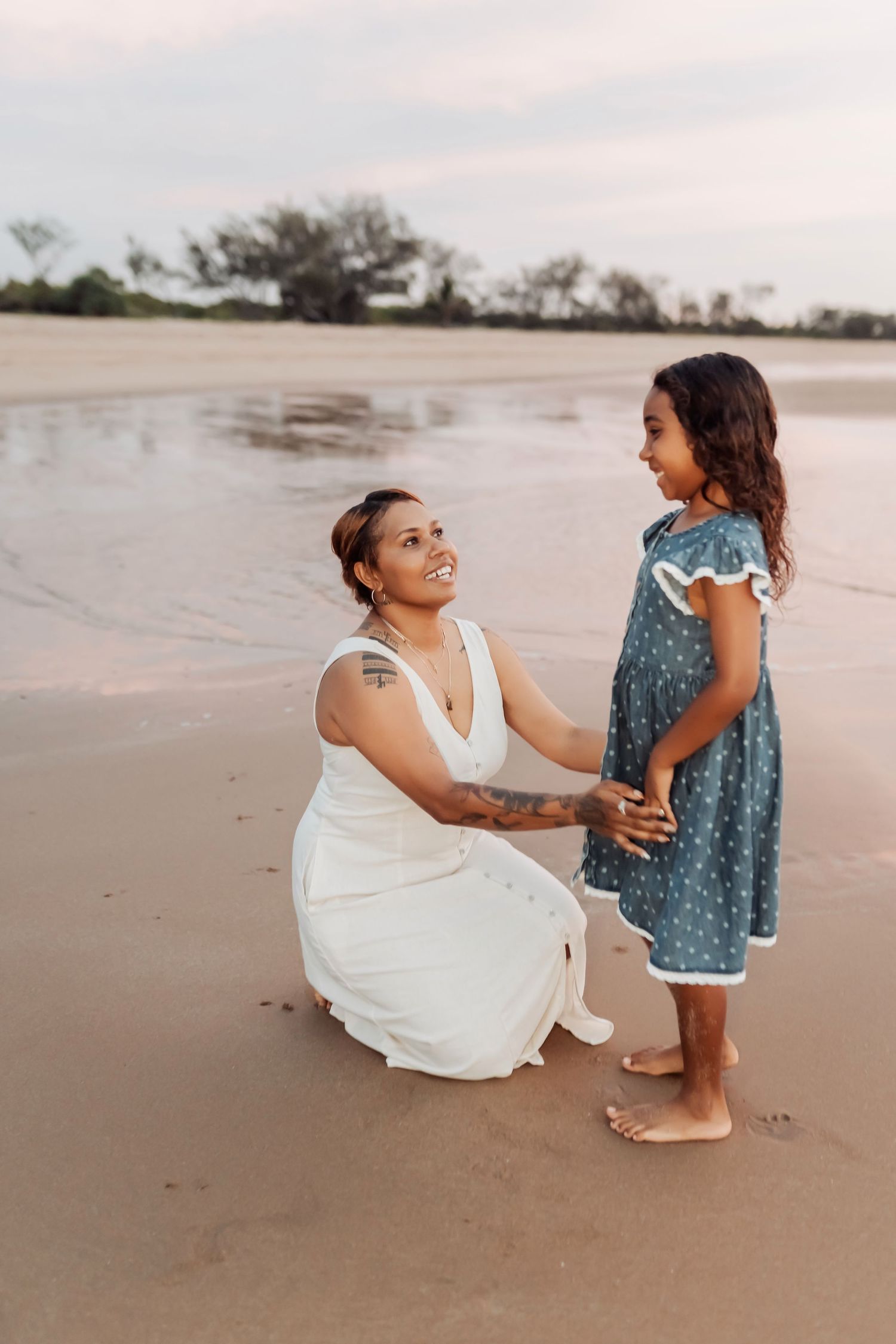 Two people in white and blue dresses playing on beach at sunset.