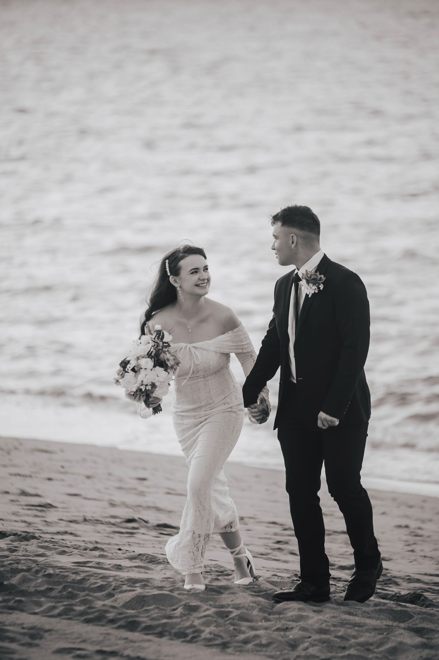 Wedding couple playfully poses on sandy beach at sunset in formal attire.