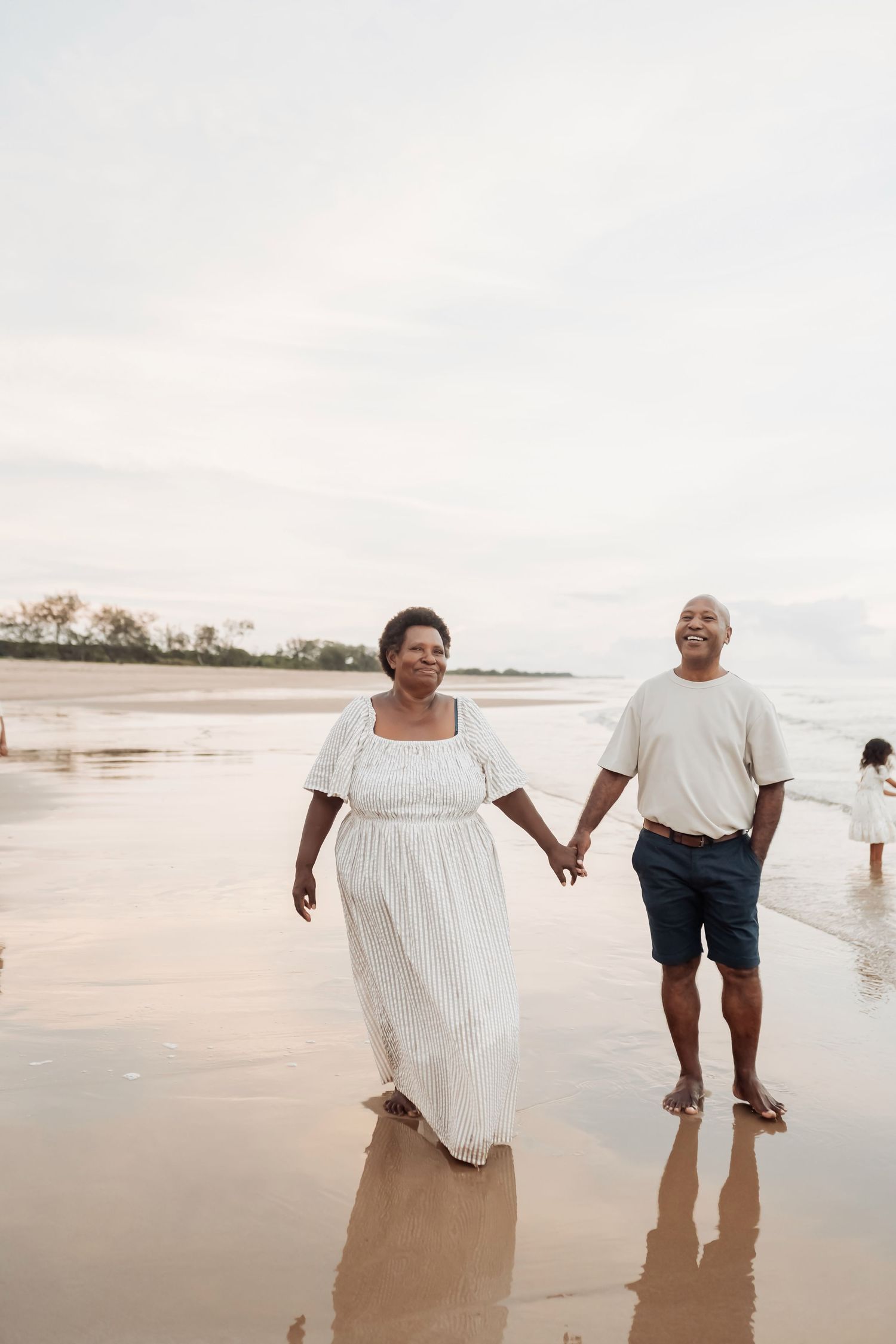 Couple holding hands while walking barefoot along the shoreline at dusk.