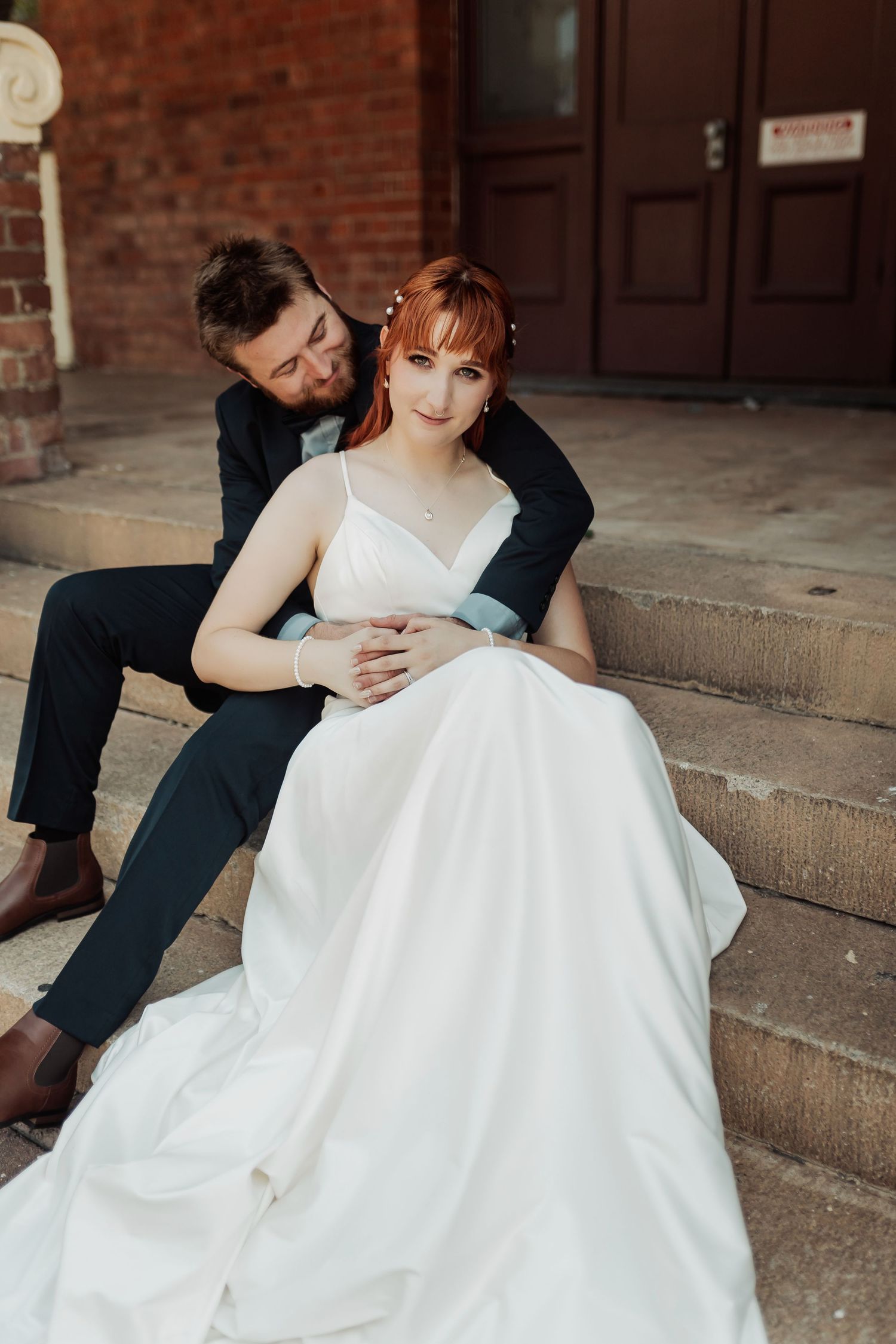 A tender embrace shared on stone steps against a brick building backdrop.