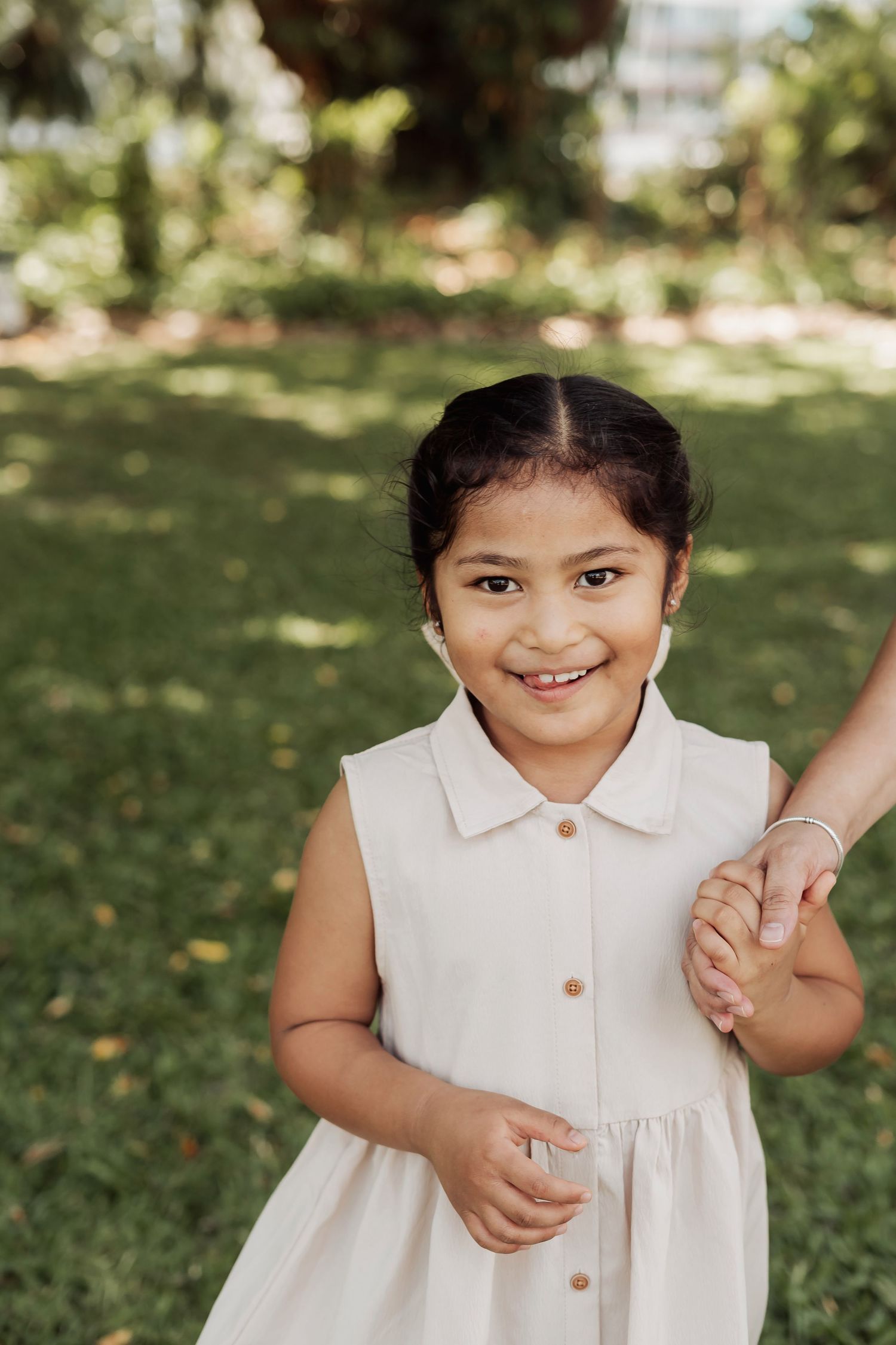 A child in a white sleeveless dress smiles joyfully while playing outdoors in a sunny garden setting.