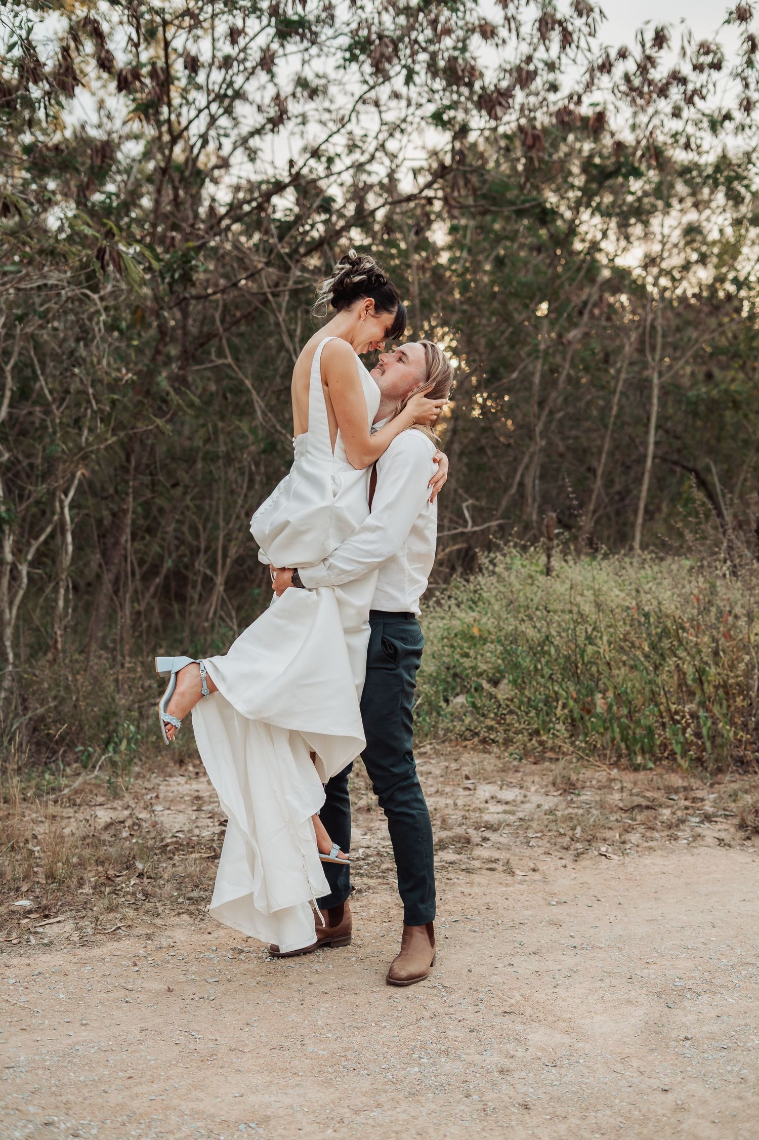 Romantic couple dancing and twirling on dirt path at sunset.