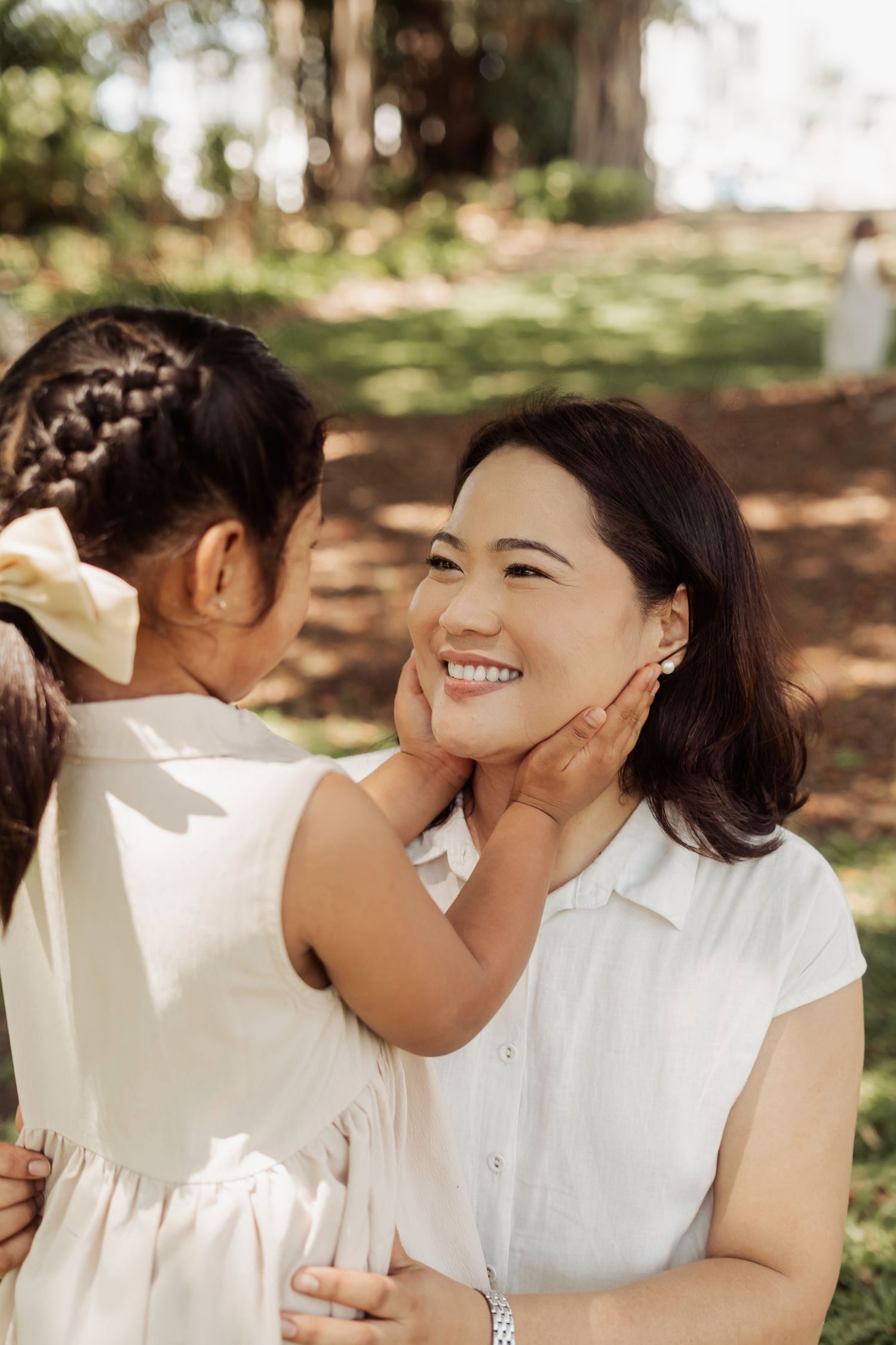 Two people wearing white outfits share tender moments together in a sunlit outdoor setting.