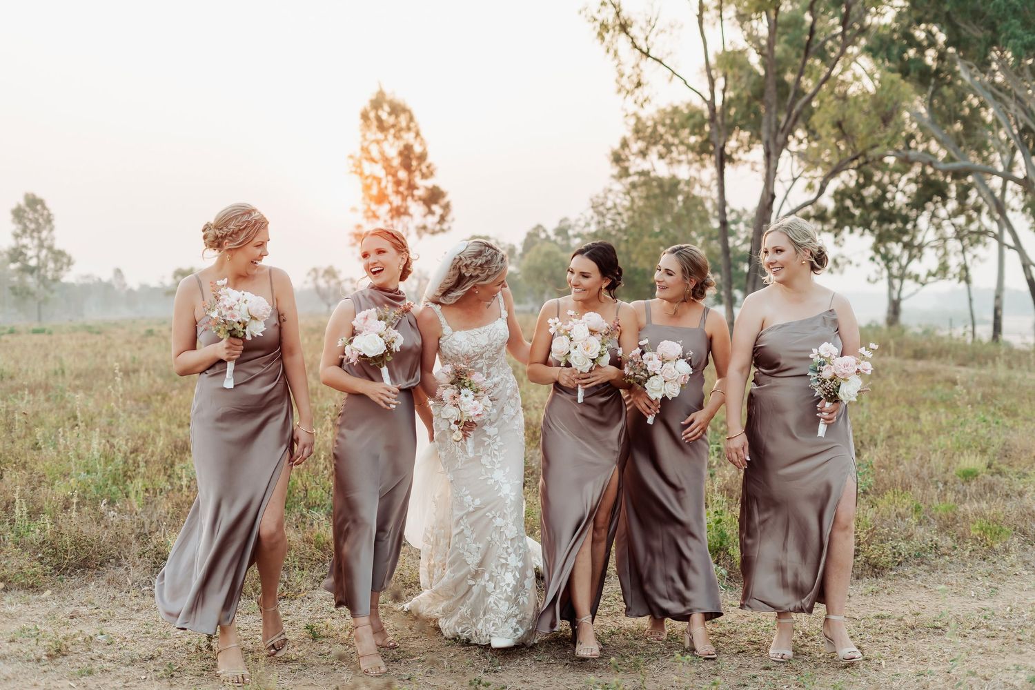 Wedding party in gray dresses poses playfully in outdoor field setting.