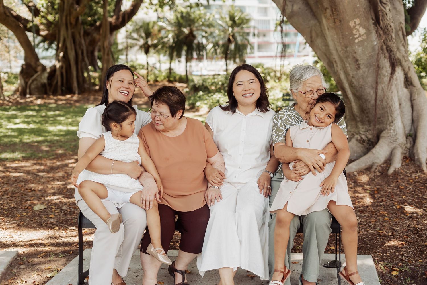 A happy family group poses together under large trees wearing coordinated casual outfits.