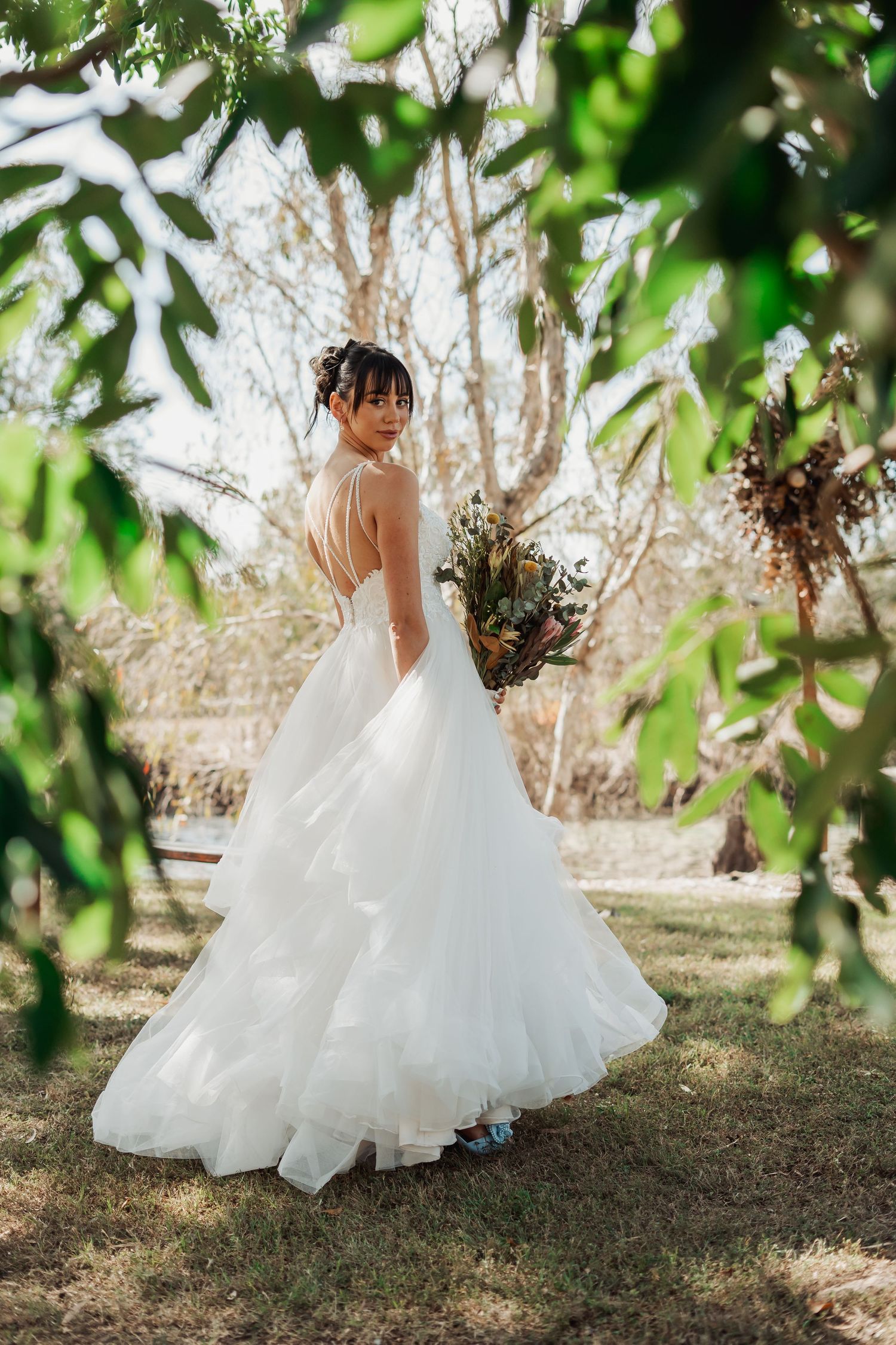 A bride in a flowing white wedding gown twirls in a garden setting framed by green leaves and natural light.
Townsville, North Queensland Au