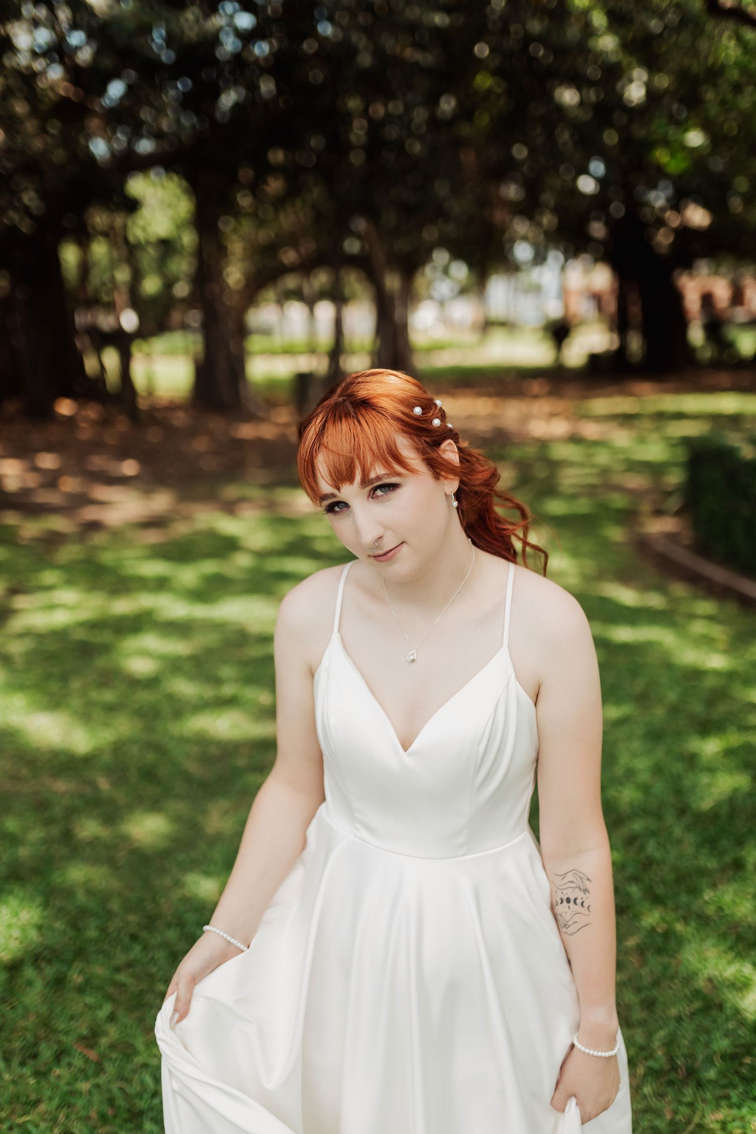 A flowing white wedding dress is showcased in a sunny outdoor garden setting.