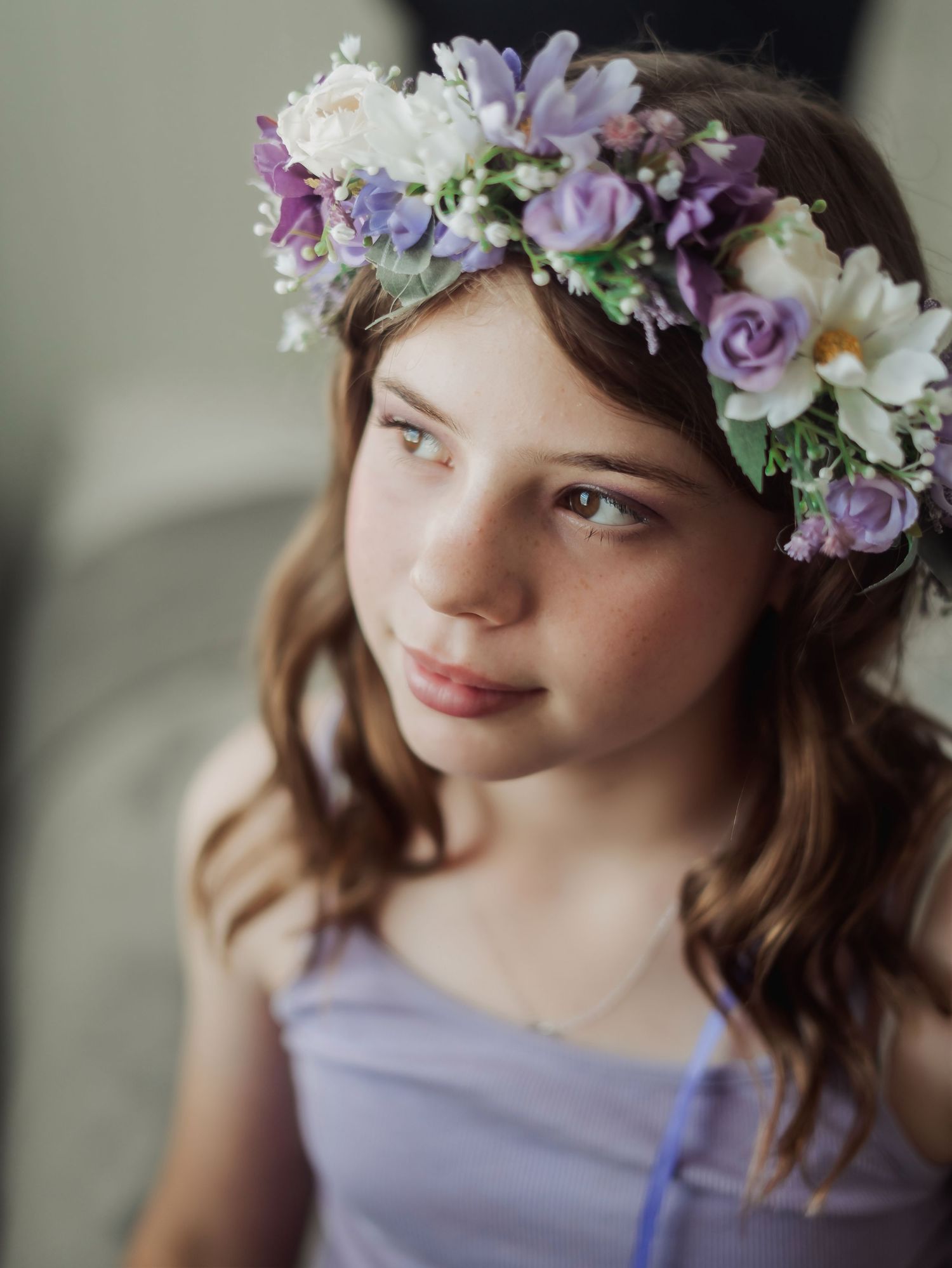 A delicate floral crown with purple and white blooms adorns a head with soft natural lighting.