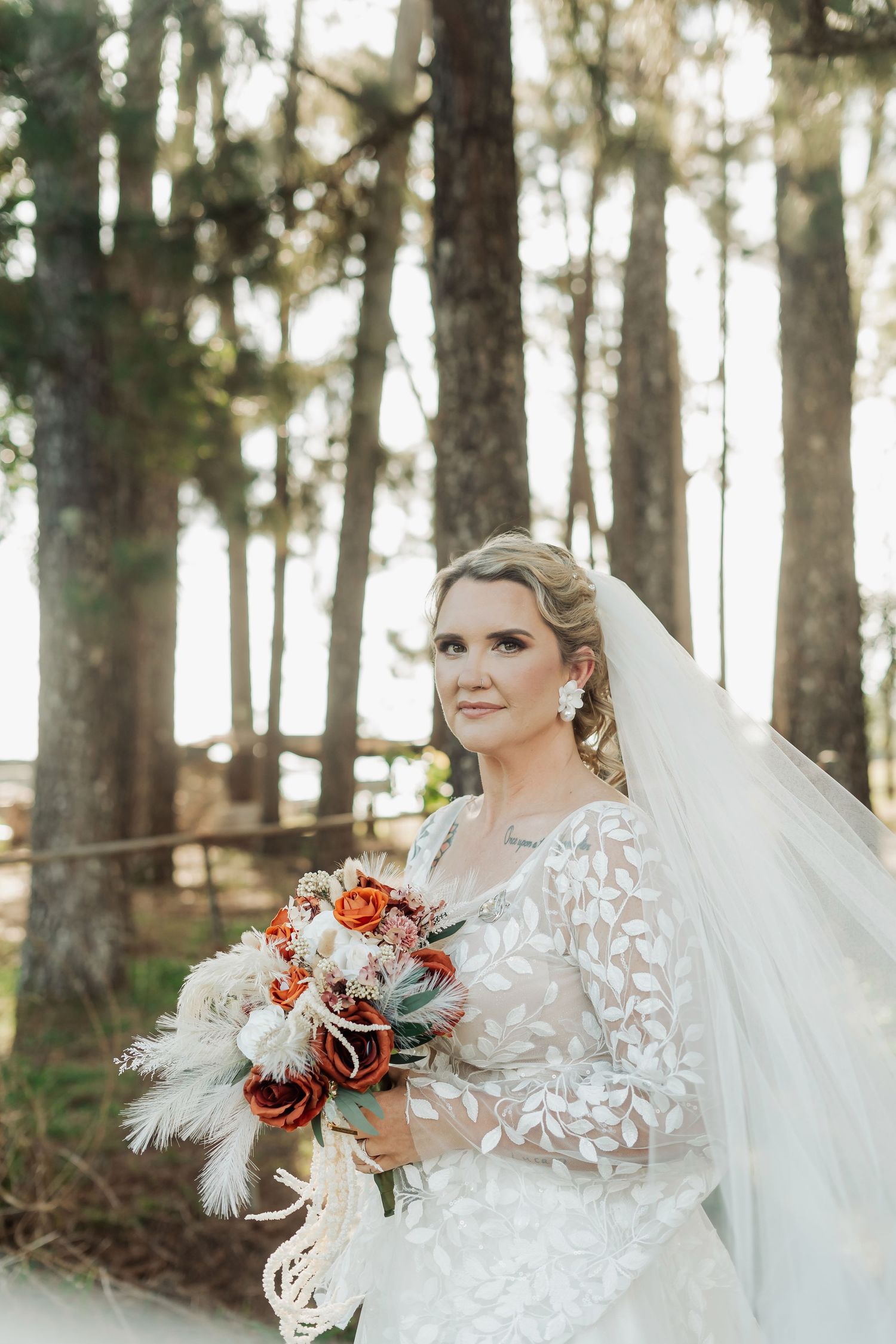 Bridal portrait in forest setting with lace dress and autumn-colored bouquet.