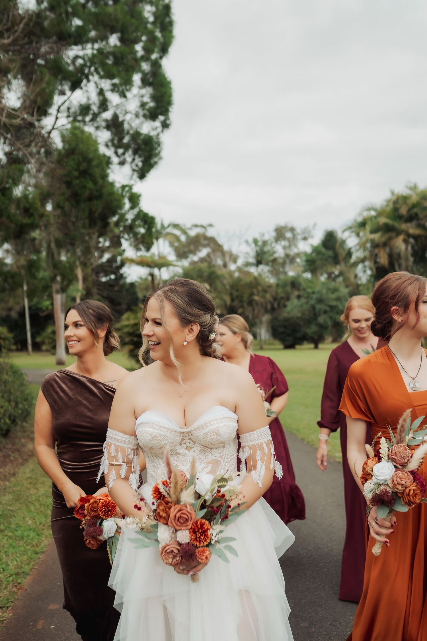 Wedding party in burgundy and rust colored dresses laughing together outdoors.