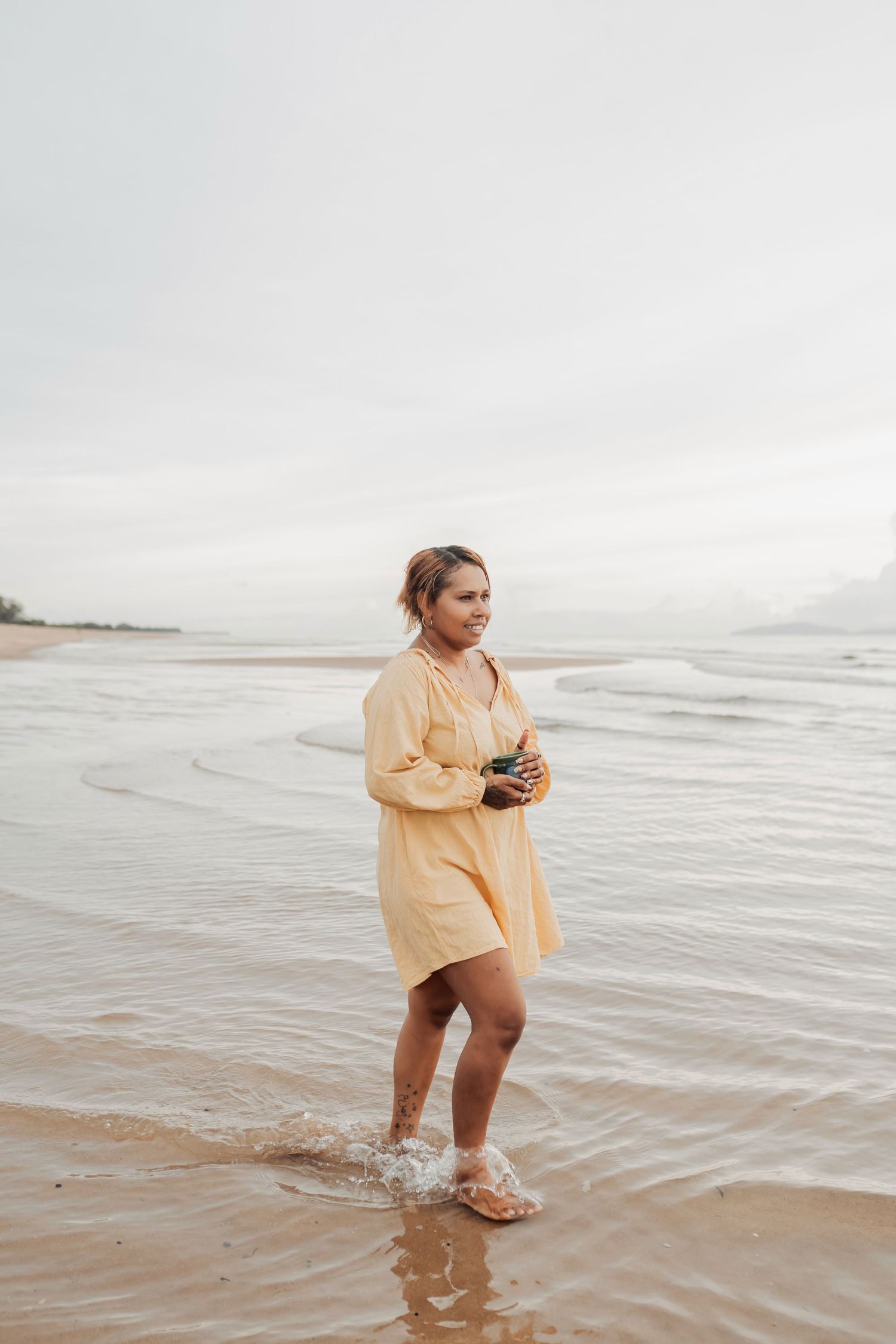 Person in yellow shirt playing in shallow ocean waves at the beach during overcast day.