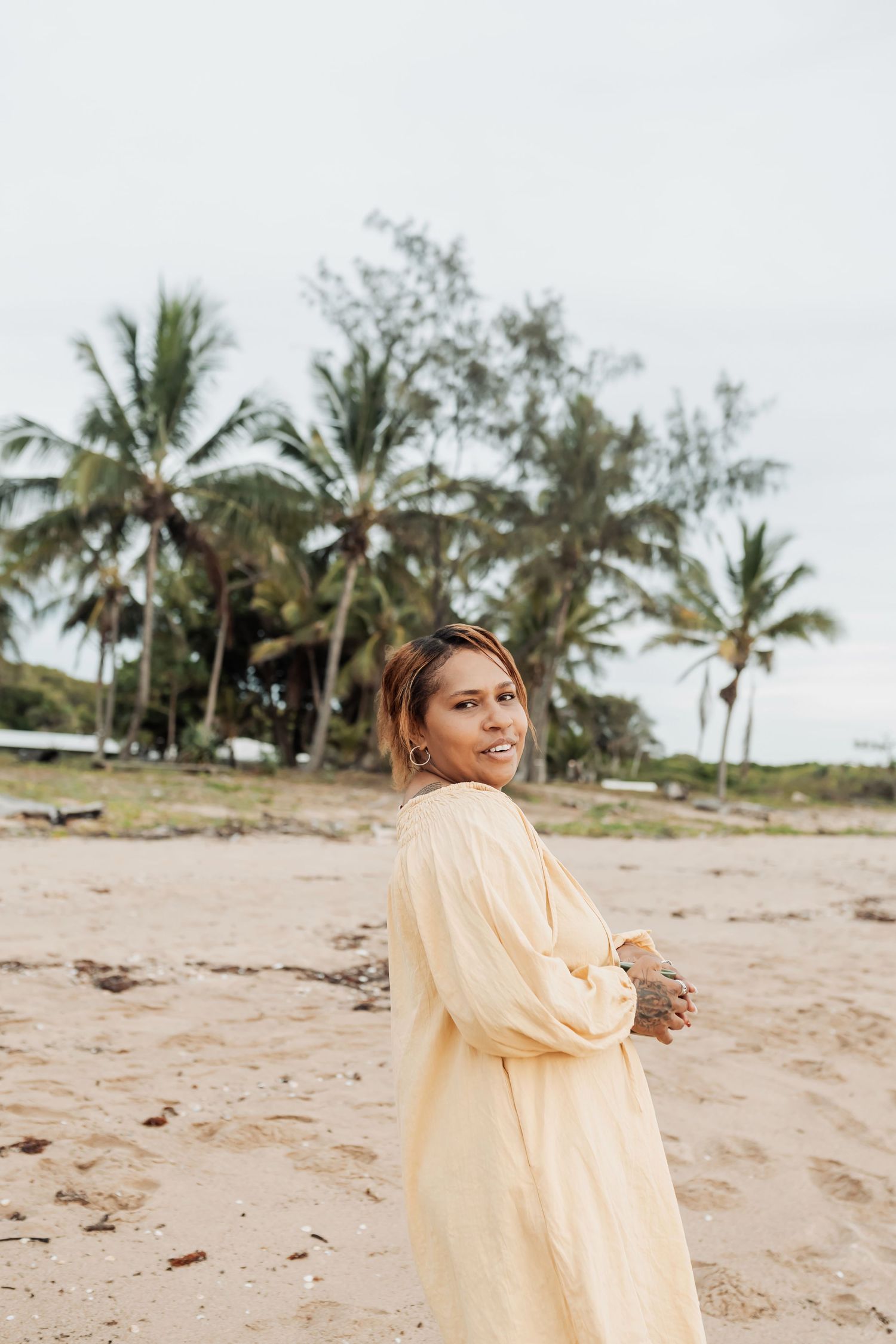 Casual beach photoshoot featuring oversized yellow shirt against palm tree backdrop.