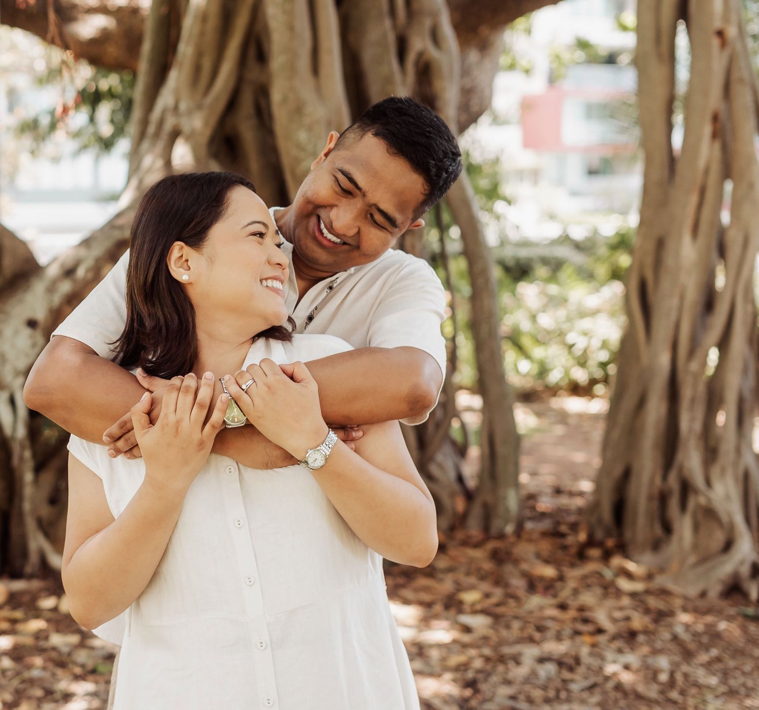 A couple shares intimate moments while embracing under a canopy of trees in a park setting.