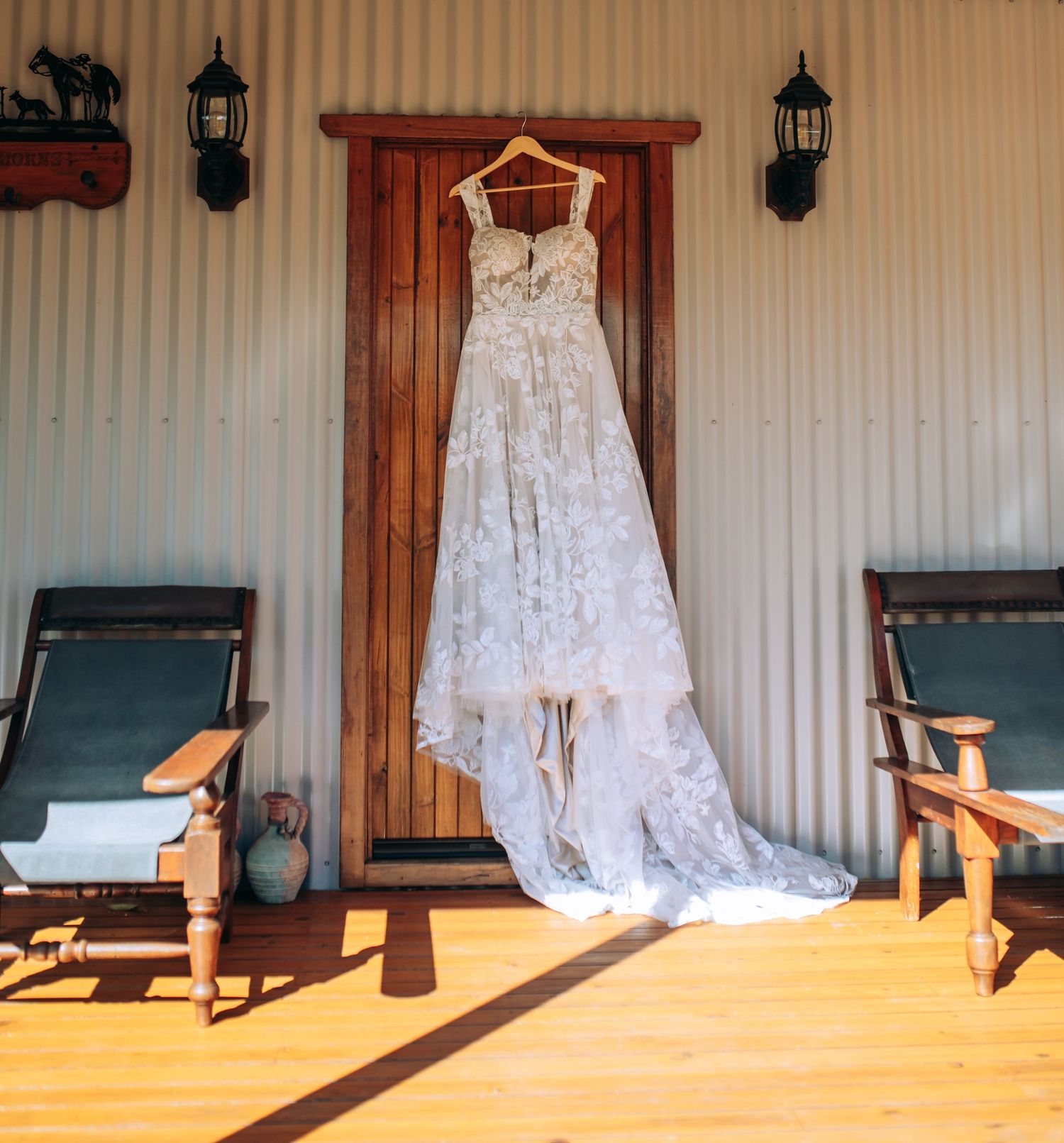 A wedding dress hangs in a rustic room with dark wooden chairs and warm lighting creating a romantic atmosphere. Long Horn, Charters Towers