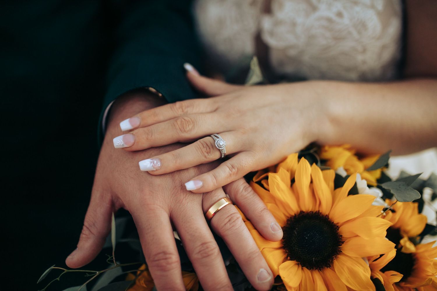 Close-up of hands wearing wedding rings with bright sunflowers in the background. Long Horns Charters Towers