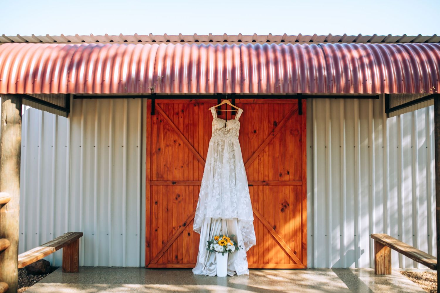 White wedding dress hanging against rustic barn doors and metal siding.
