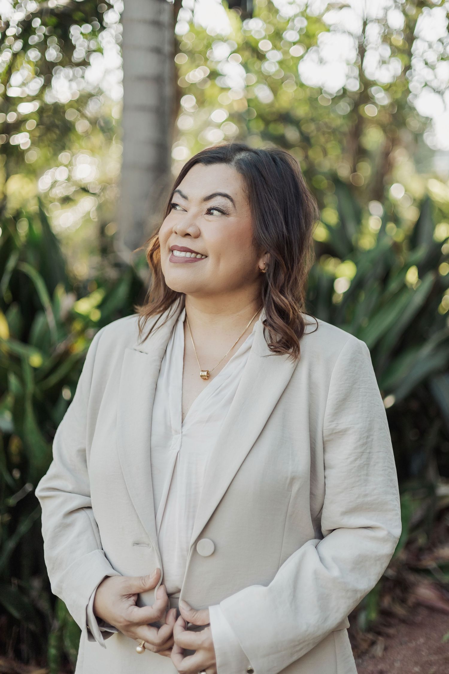 Professional portrait of woman in cream blazer laughing against tropical garden background.