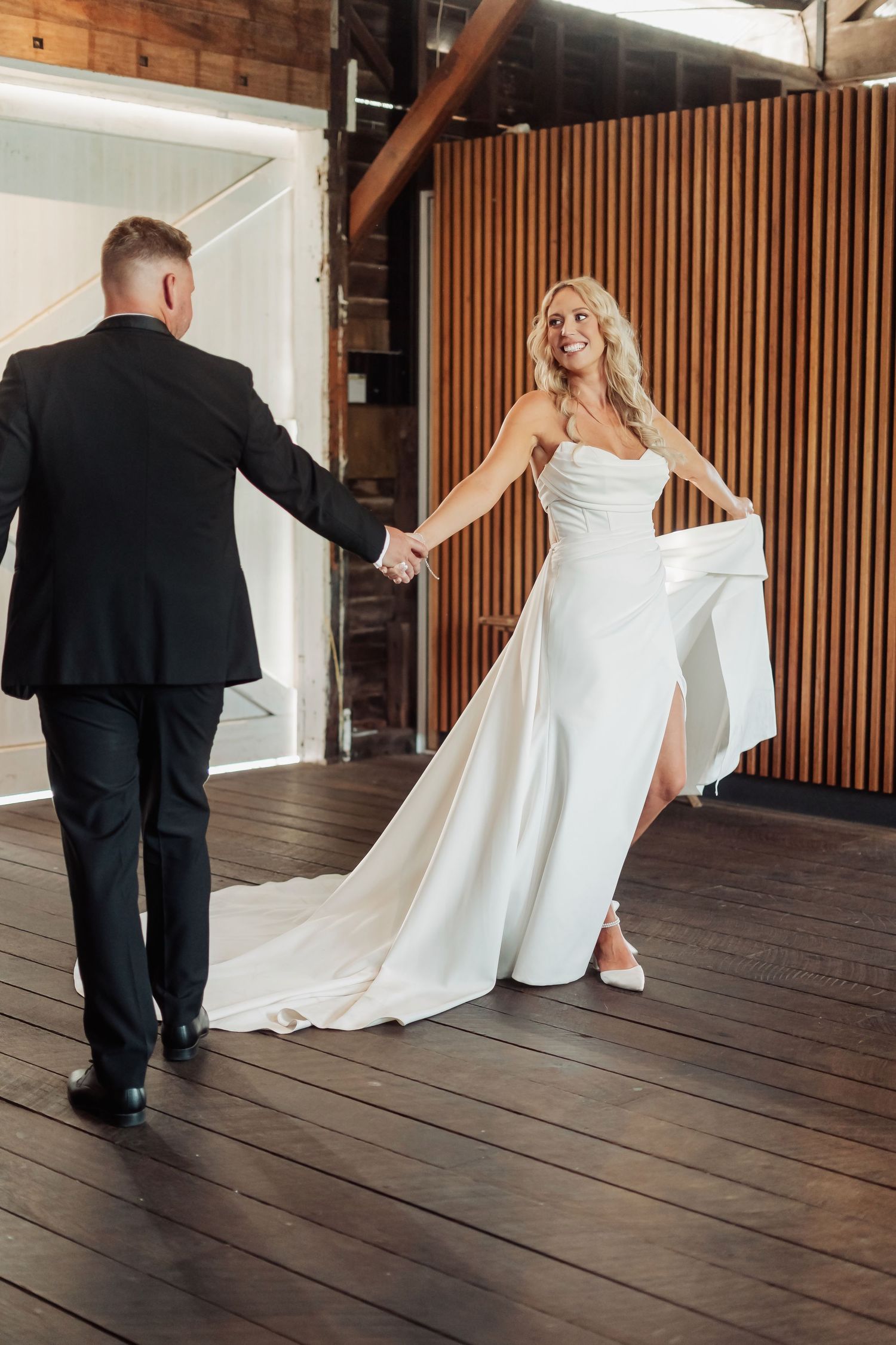Wedding couple twirls and dances together on a wooden deck with vertical wood paneling in the background.