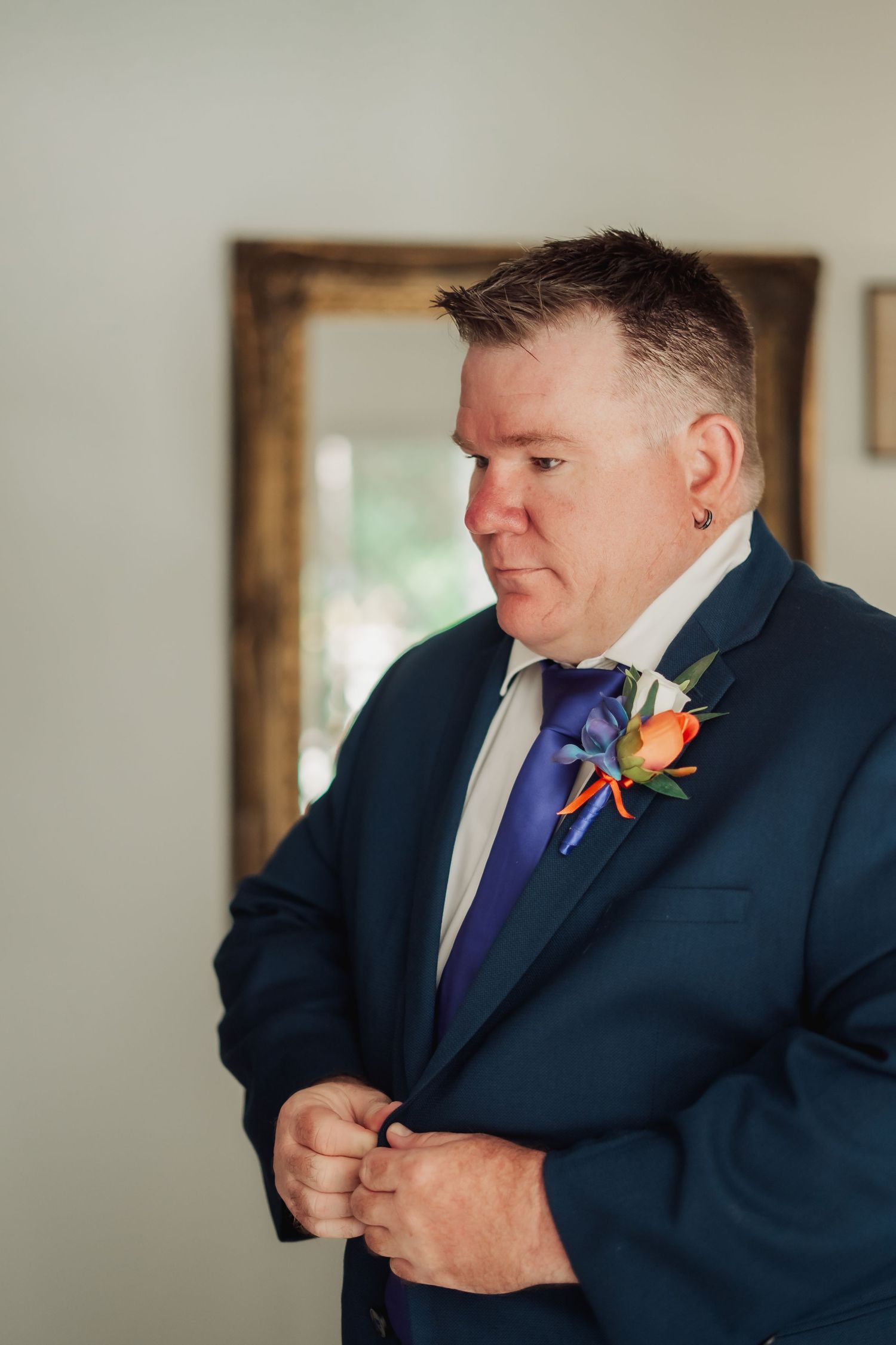 A person in a navy suit adjusts their boutonniere while getting ready for a formal event.
