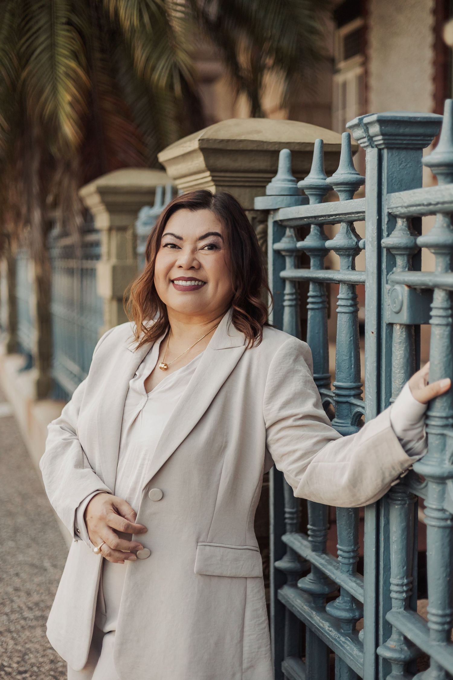Professional portrait session with beige blazer against ornate blue railing and stone architecture.