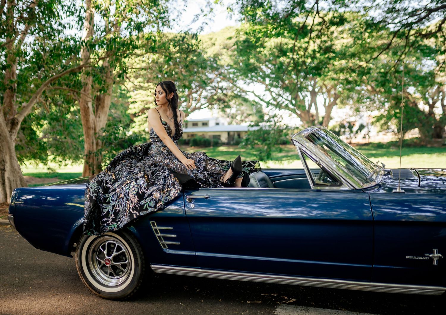 Classic navy blue convertible car photographed in a lush garden setting.